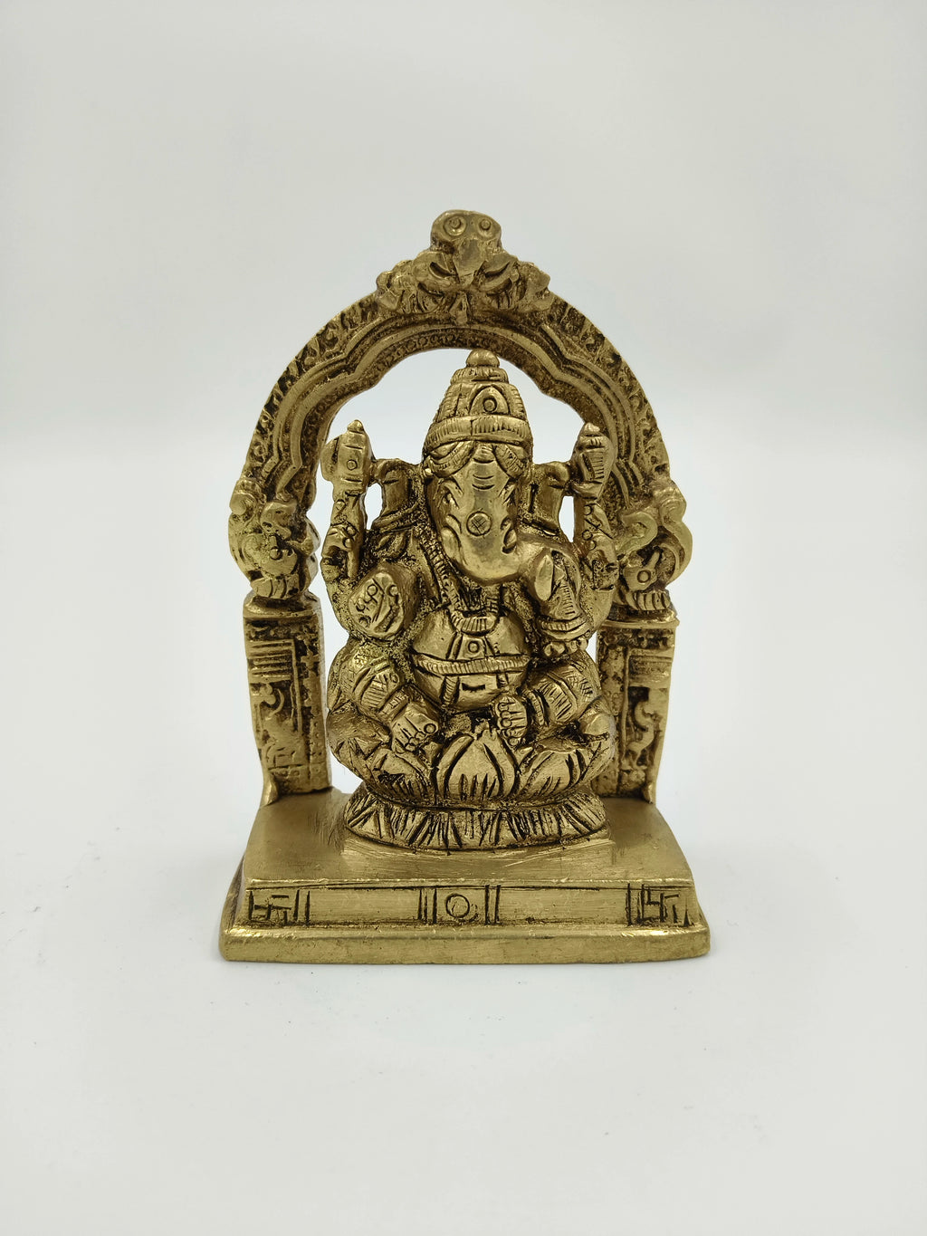 Small brass sculpture of Lord Ganesha seated with decorative arch on base