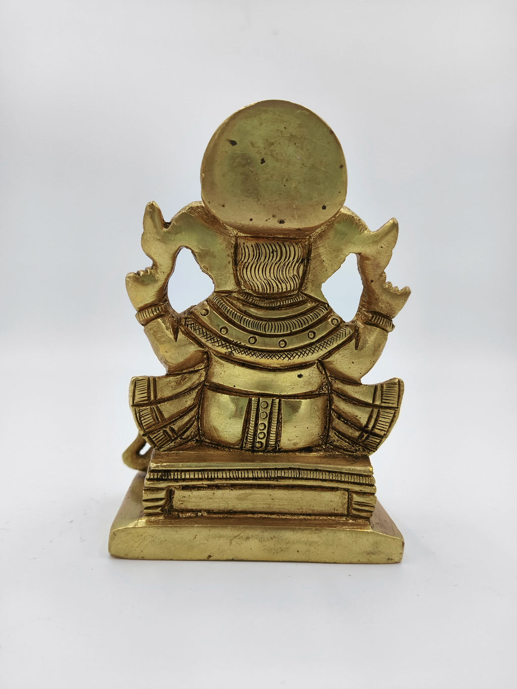 Back view of small brass Siddhi Vinayaka statue sitting on a pedestal