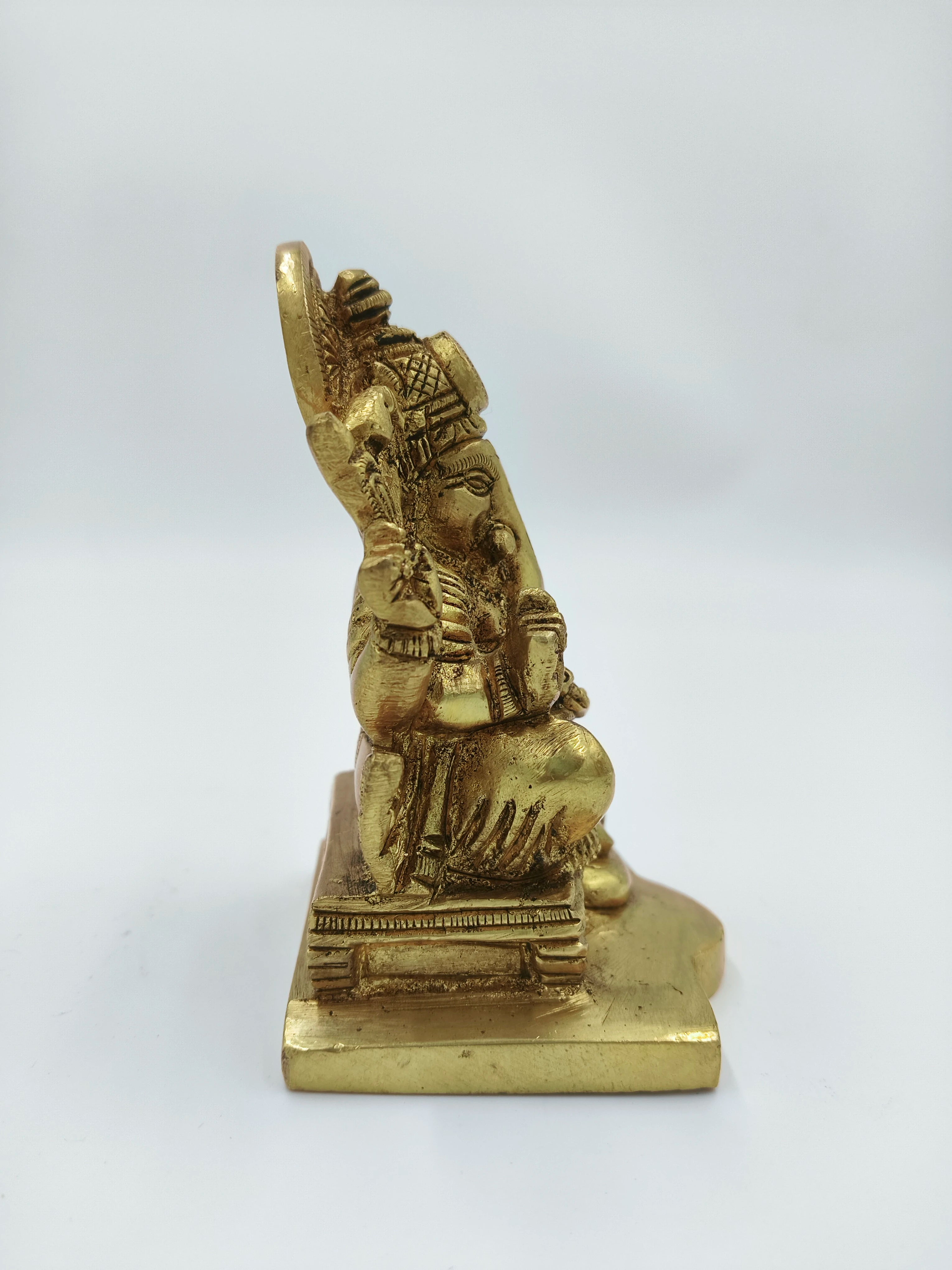 Side view of small brass Siddhi Vinayaka statue seated on a pedestal