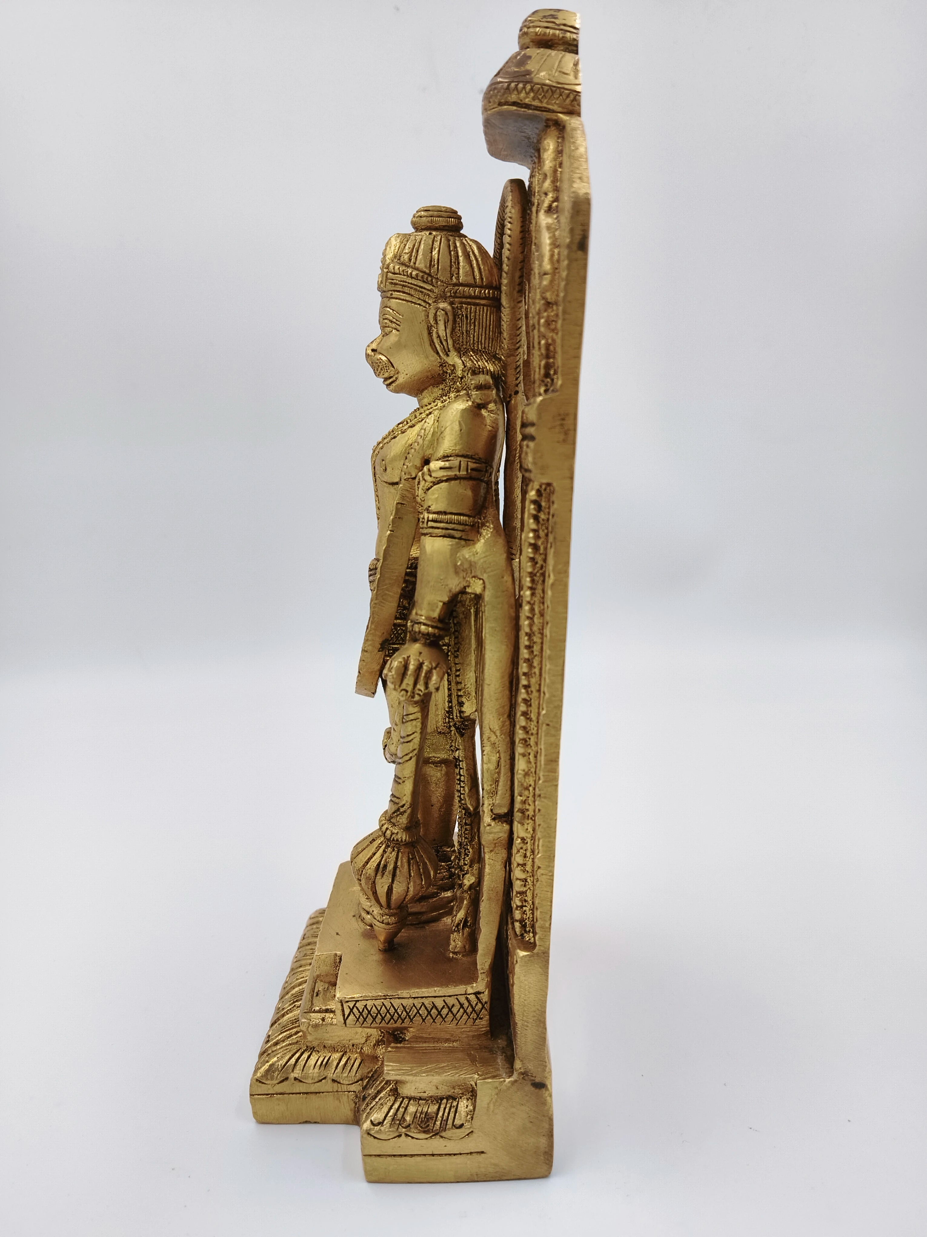 Side view of brass standing Hanuman sculpture with ornate backing