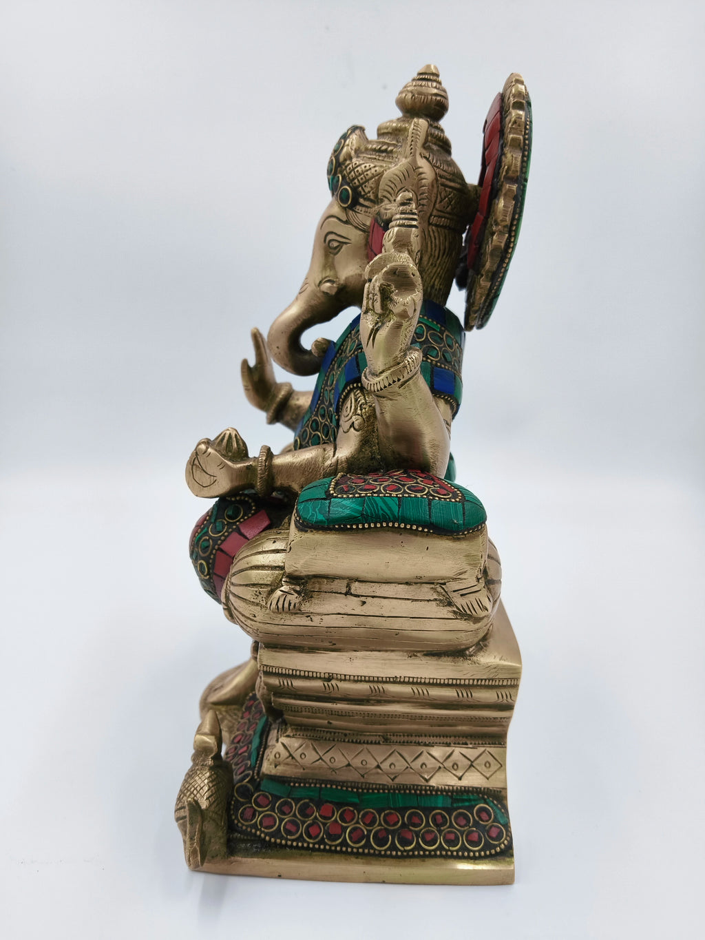 Side view of large brass Ganesh statue with colorful accents sitting on ornate base