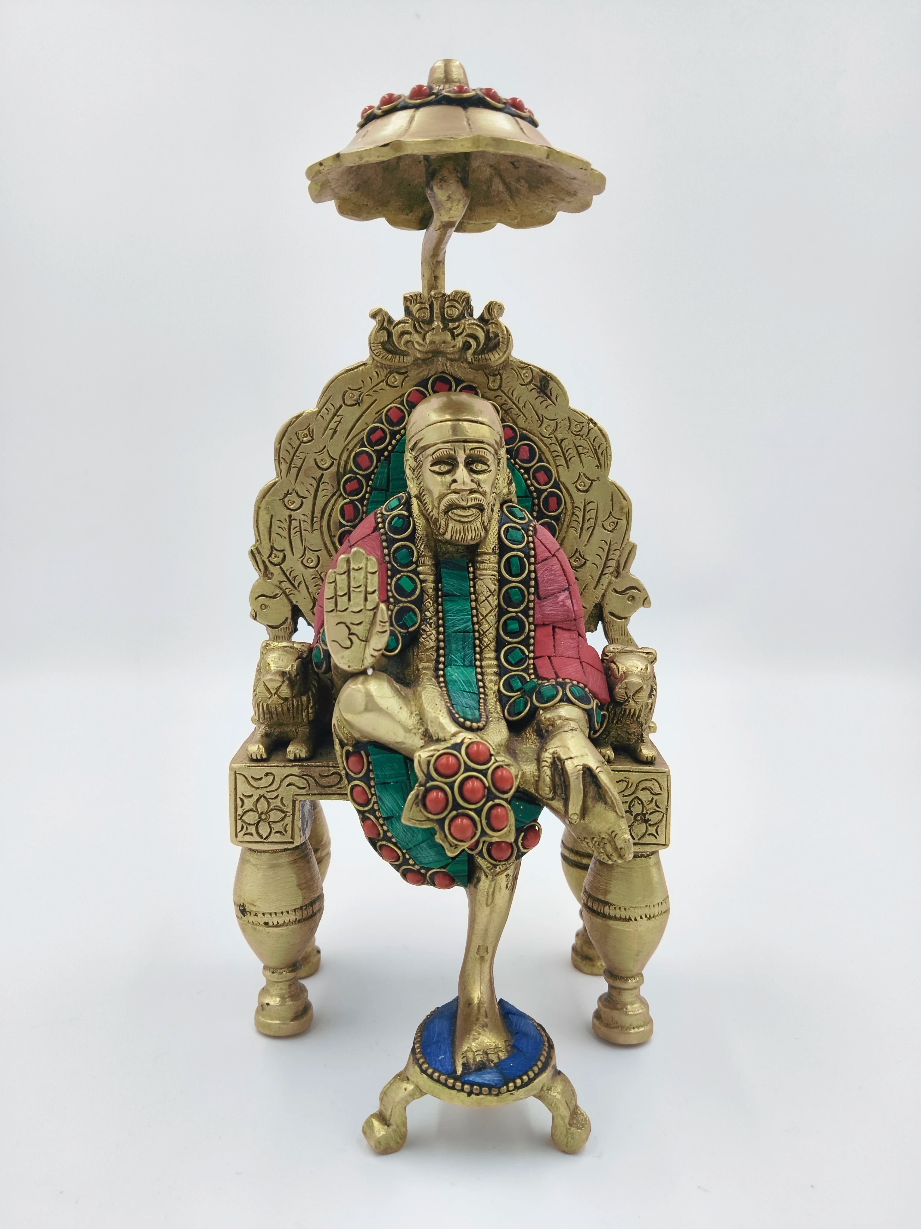 Brass statue of Shirdi Sai Baba sitting on an ornate throne with multicolored accents