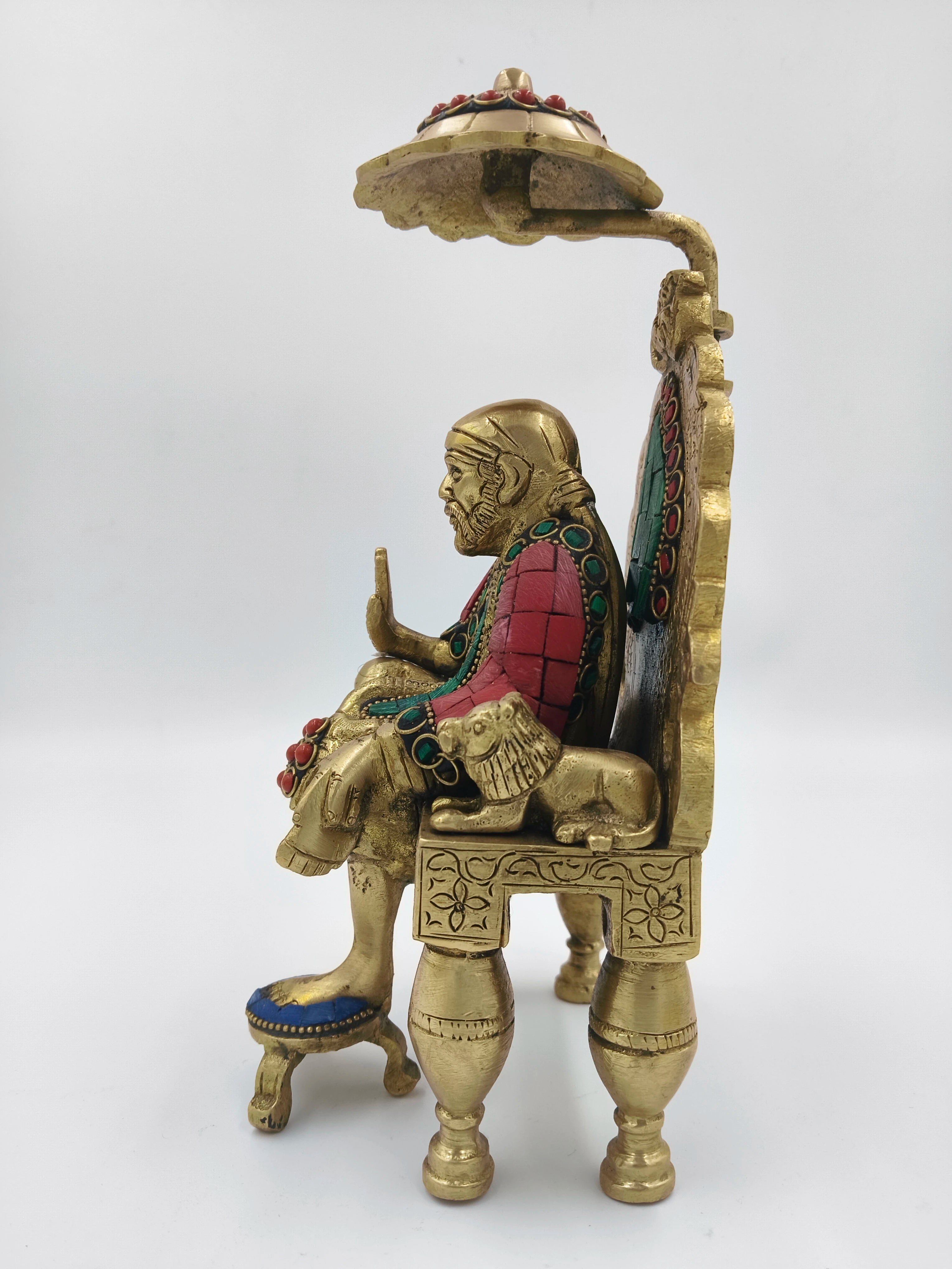 Side view of brass Shirdi Sai Baba statue sitting on decorated simhasan throne