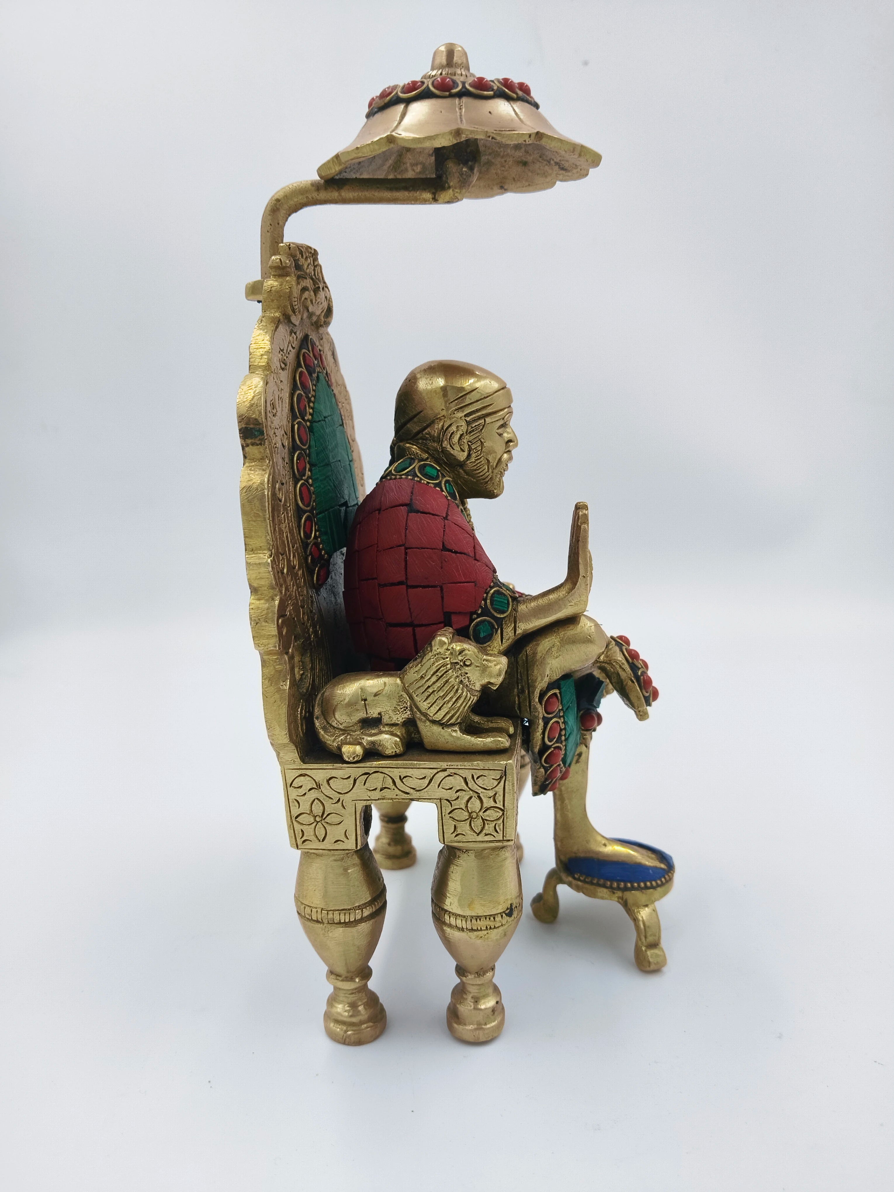 Side view of brass Shirdi Sai Baba statue sitting on decorated throne with umbrella