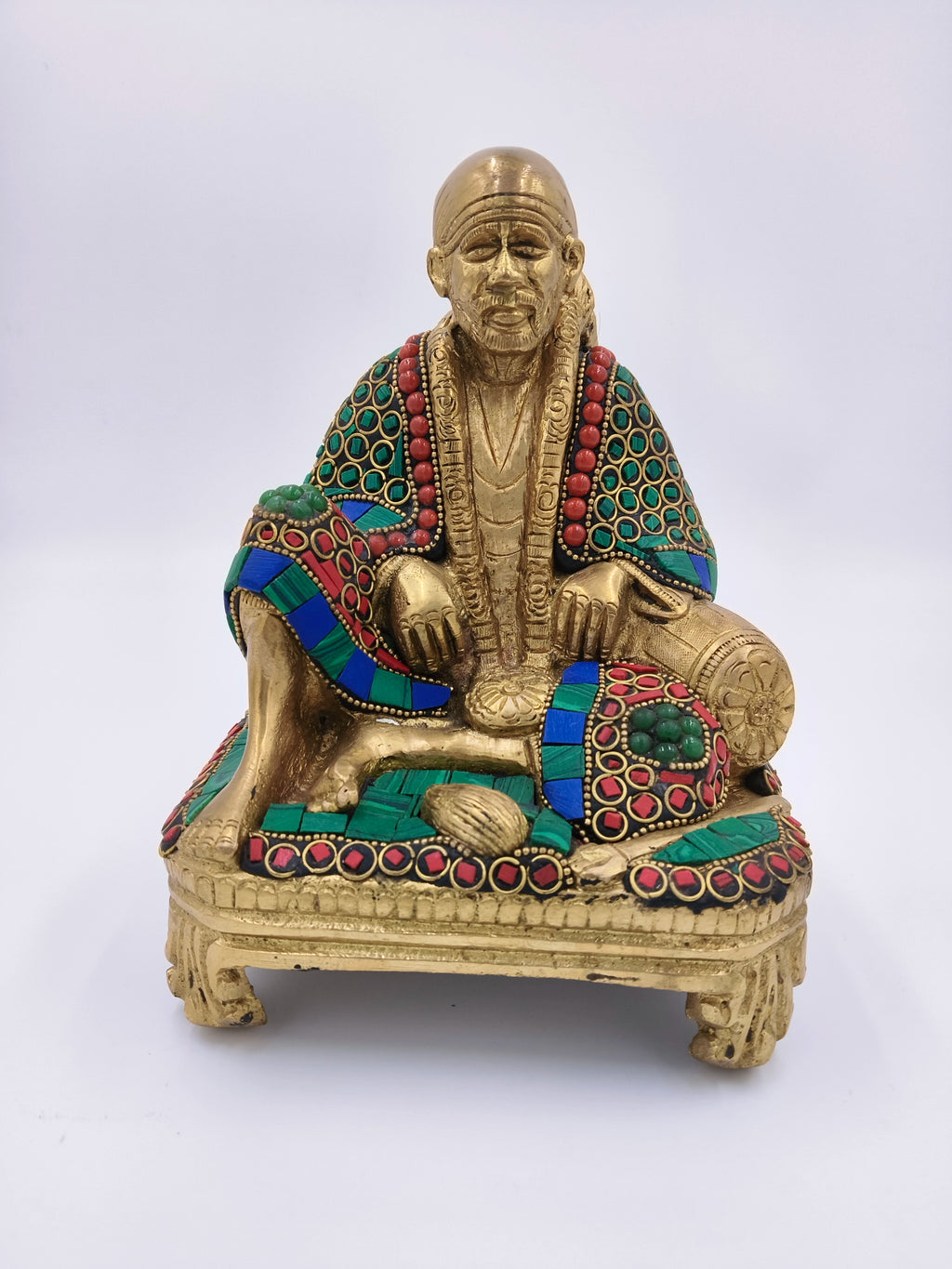 Large brass statue of Shirdi Sai Baba sitting on a chowki with colorful embellishments