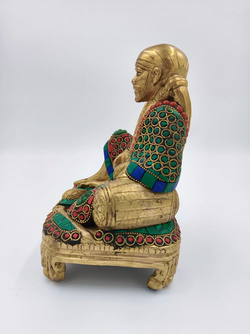 Side view of a large brass statue of Shirdi Sai Baba sitting on a decorated chowki