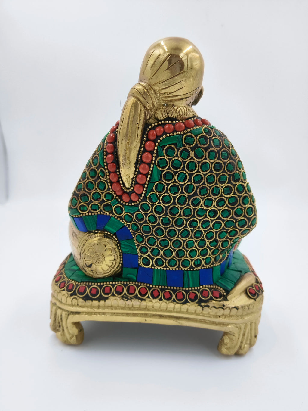 Back view of brass Shirdi Sai Baba statue seated on a decorated chowki