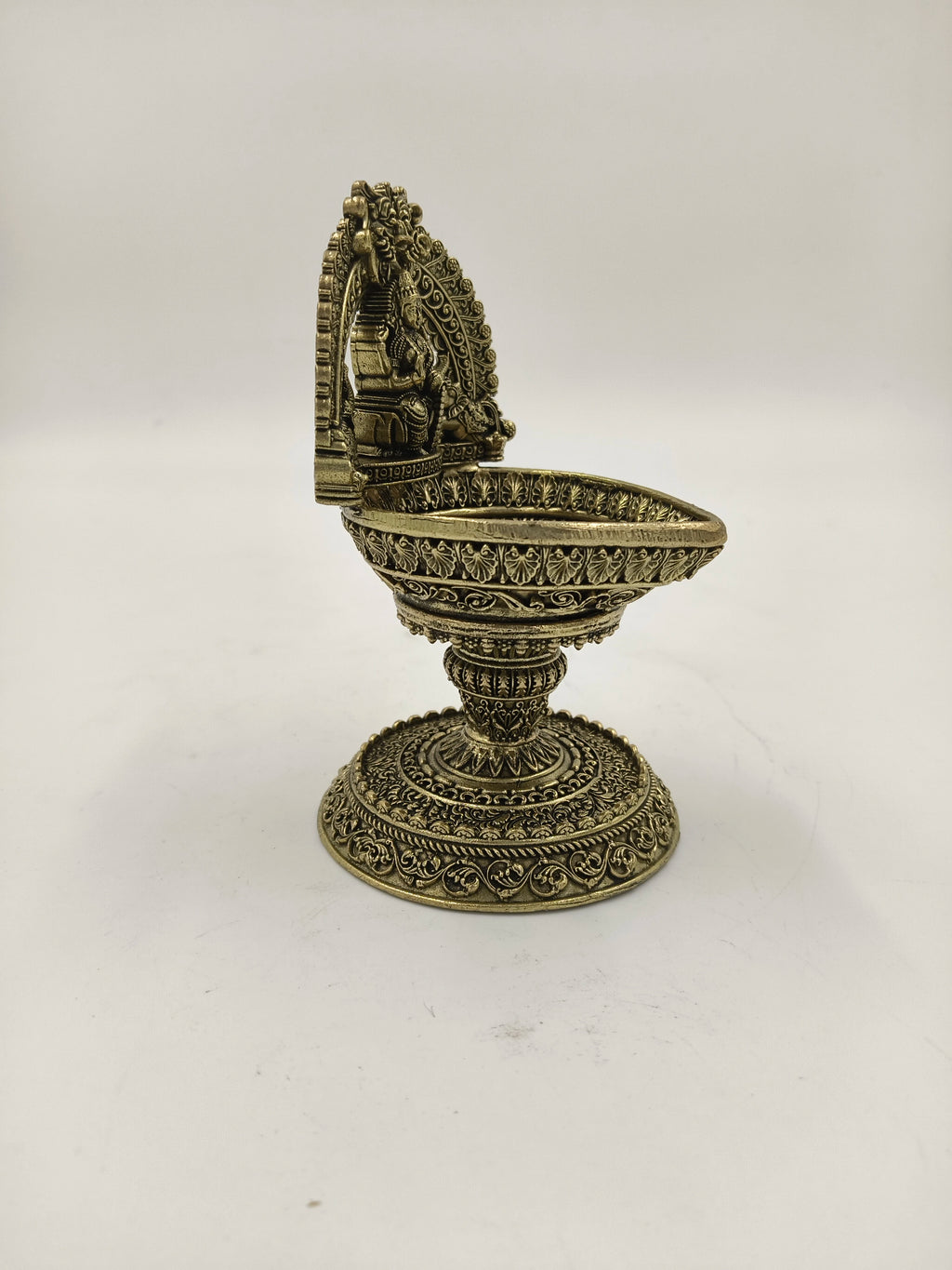 Side view of a medium brass Lakshmi deep with intricate arch and base details