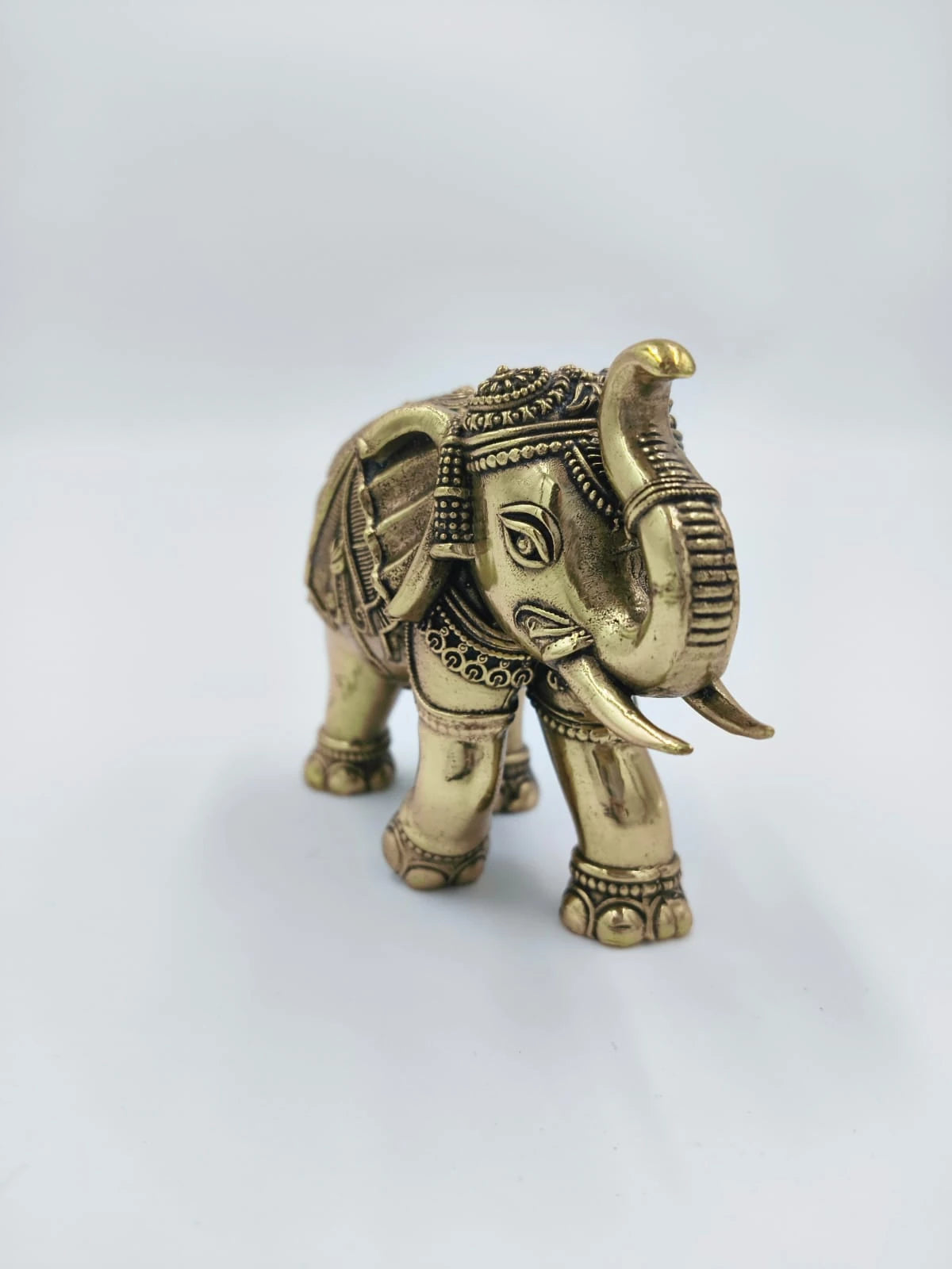 Small brass elephant figurine with intricate detailing on a white background