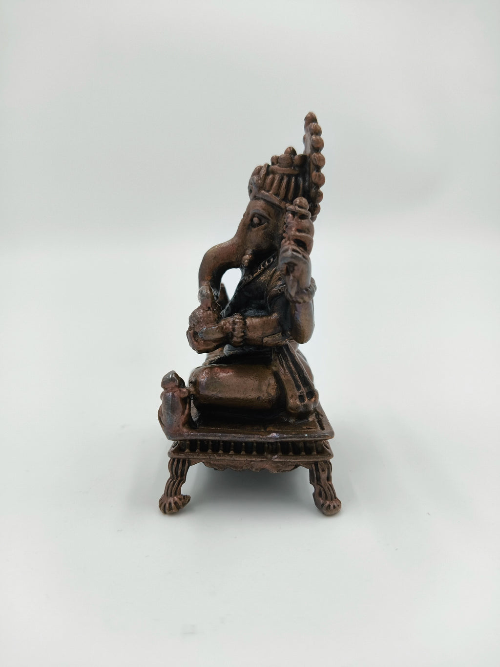 Side view of copper Hindu deity Ganesh seated on a decorative chowki