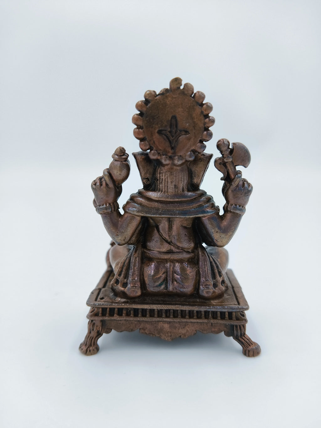 Back view of a copper Ganesh statue seated on a decorative chowki platform