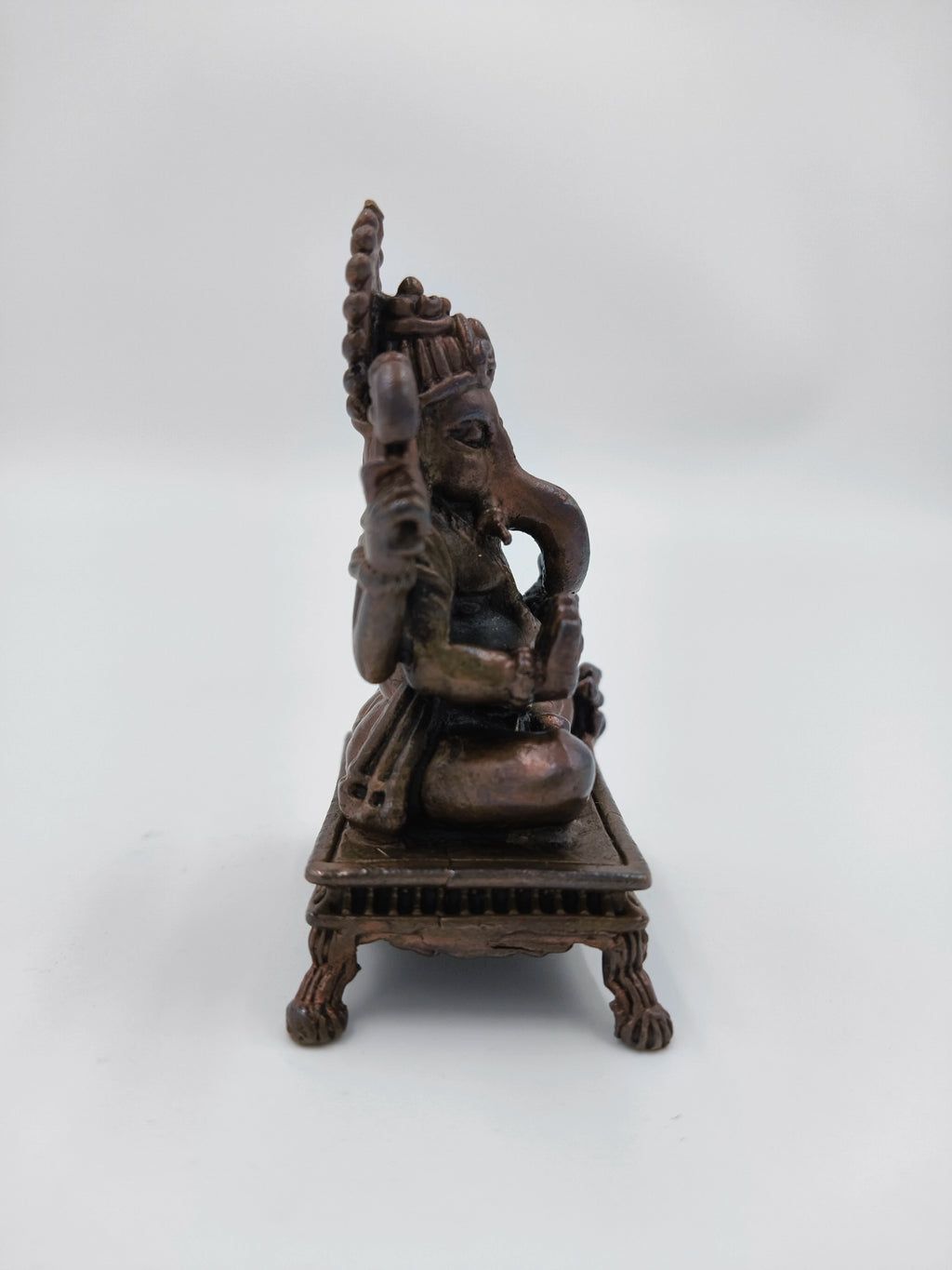 Side view of a small copper Ganesh statue seated on a decorative chowki