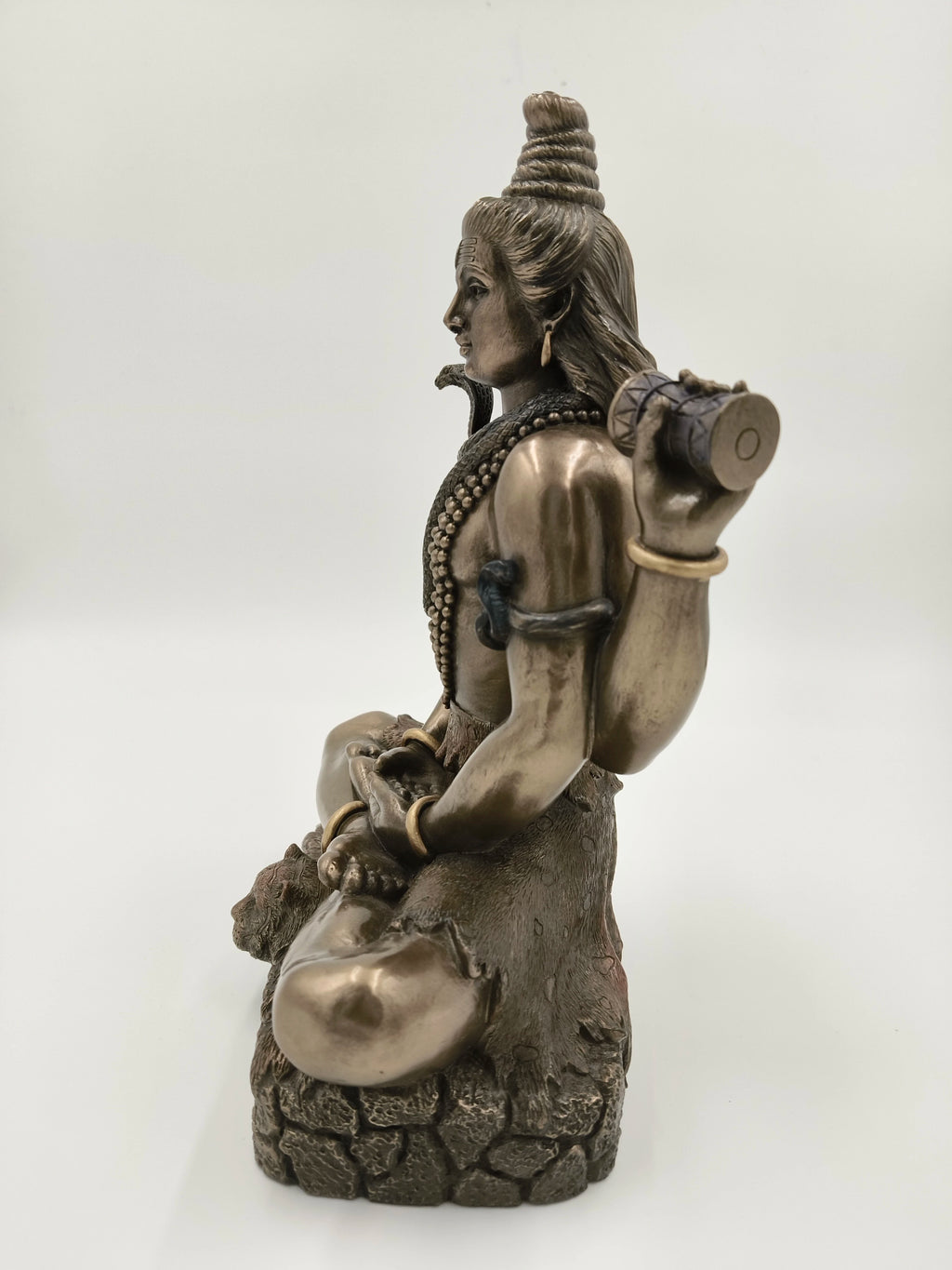 Side view of polyresin sculpture of Hindu deity Shiva seated with damaru drum