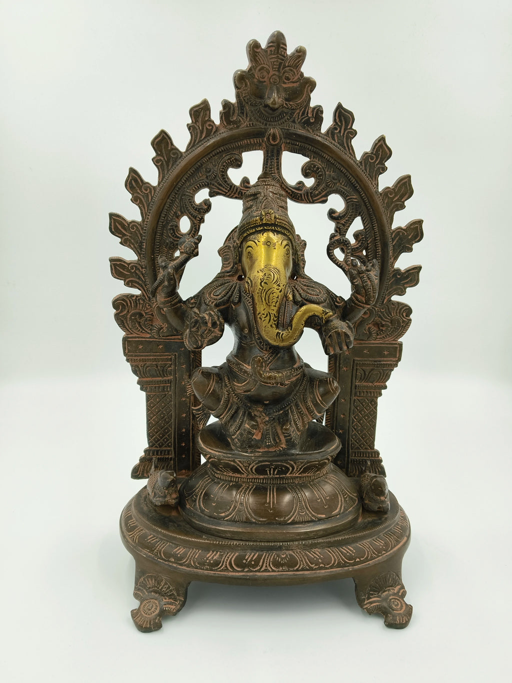 Large brass sculpture of Ganesh sitting under decorative arch