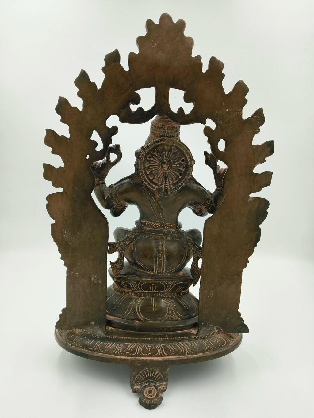 Back view of large brass Ganesh statue seated within an arch with detailed carvings