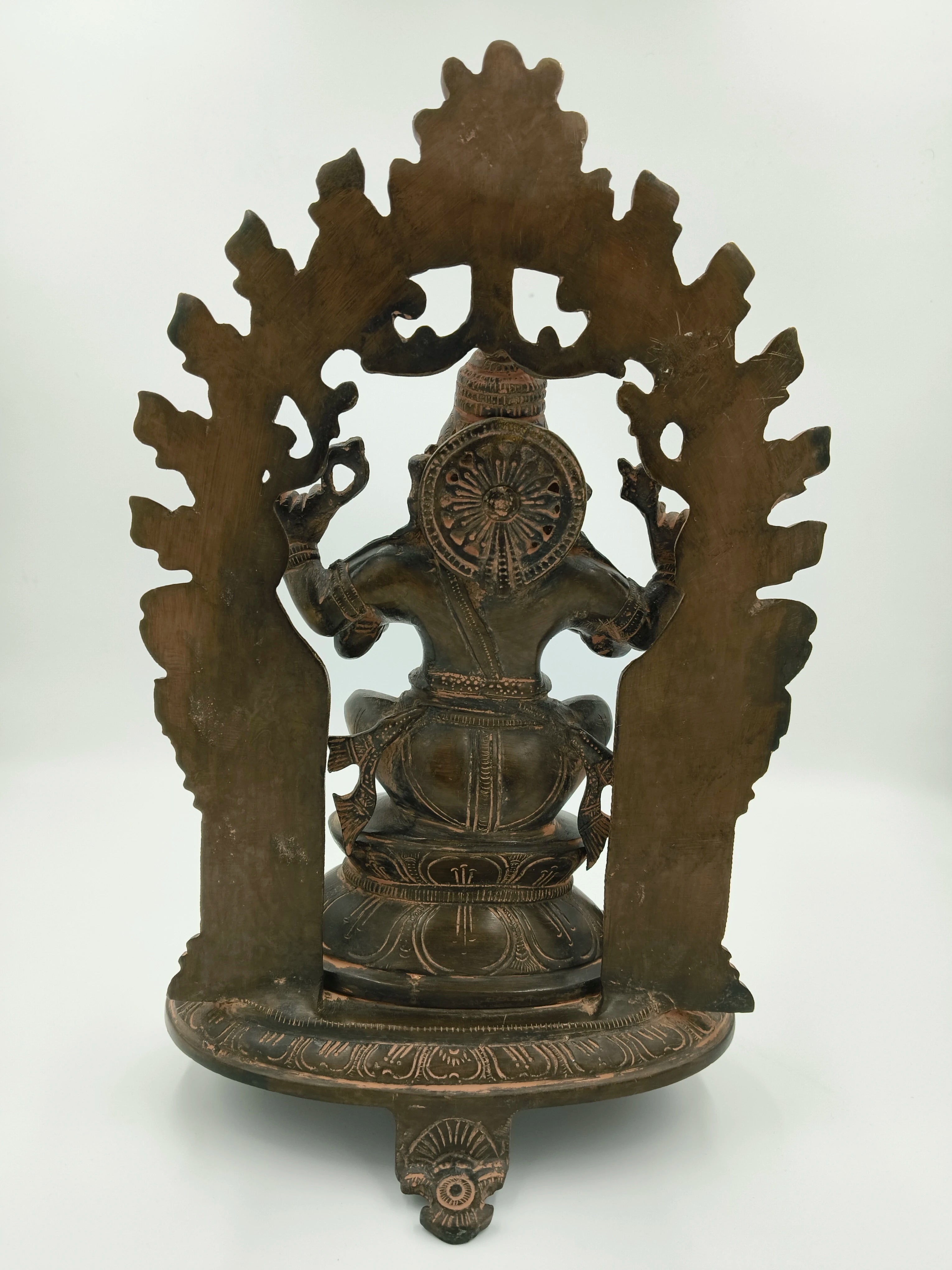 Back view of large brass Ganesh statue seated within an arch with detailed carvings