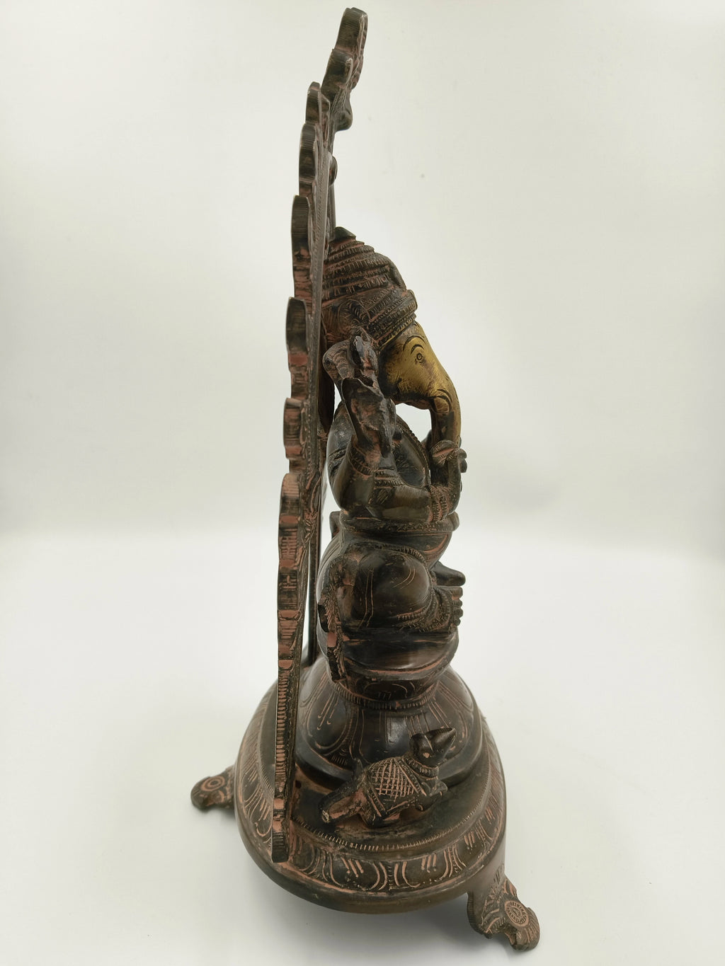 Side view of a large brass sculpture of Ganesh with decorative arch and mouse base