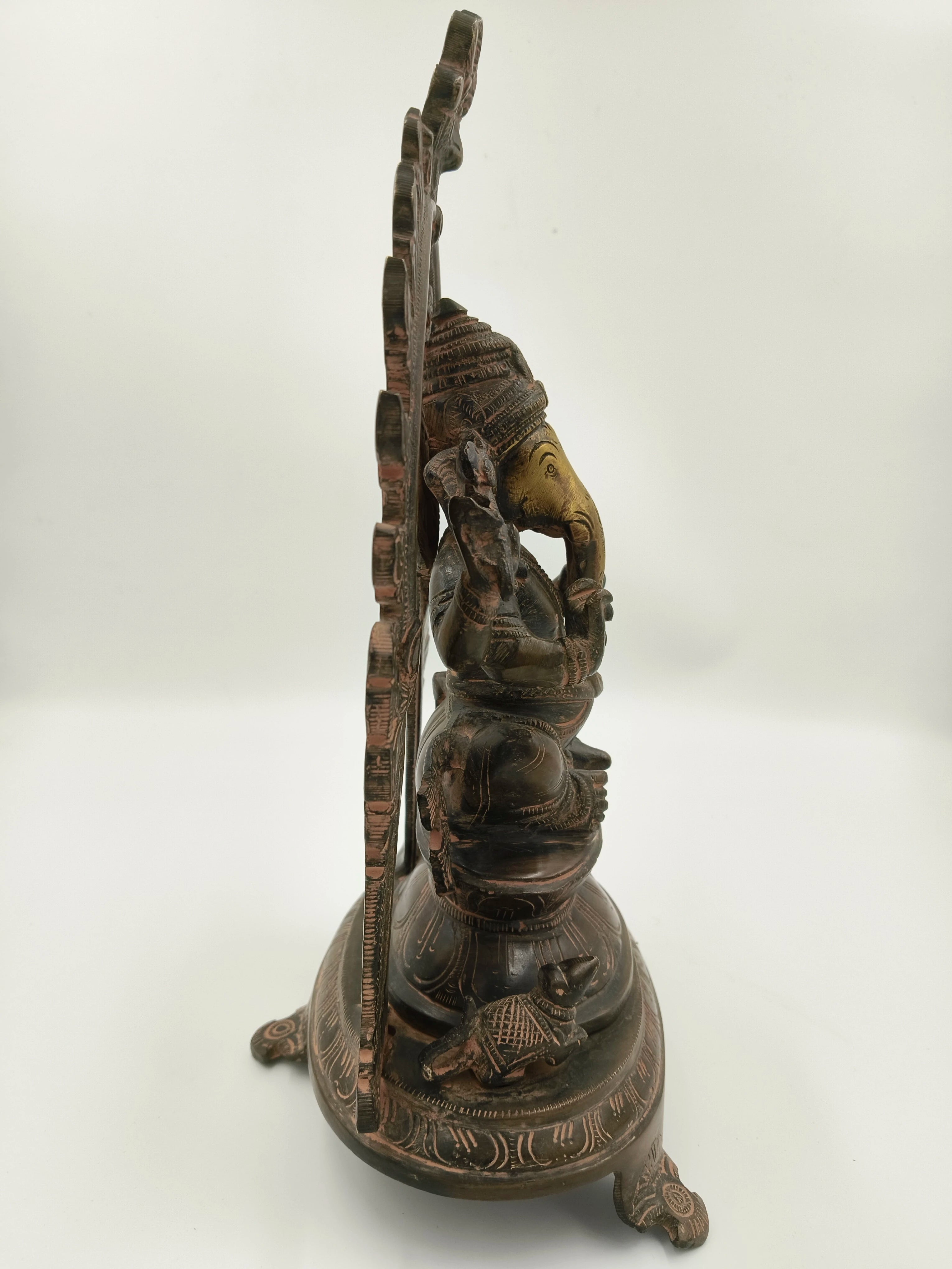 Side view of a large brass sculpture of Ganesh with decorative arch and mouse base