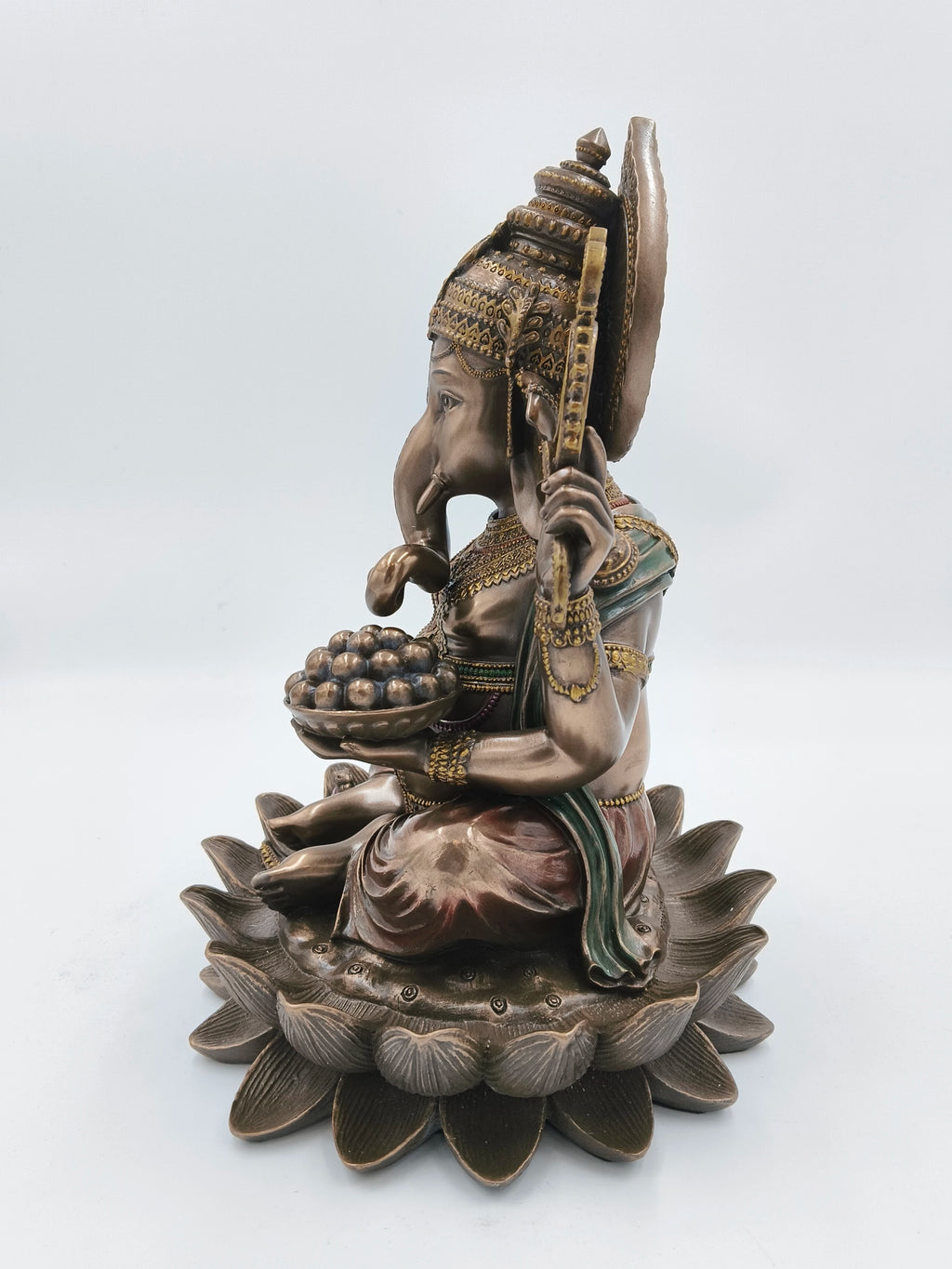 Side view of polyresin Ganesh idol sitting on a lotus base with decorative details