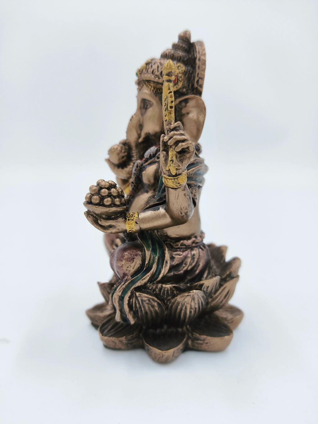 Side view of small polyresin Ganesh statue sitting on a lotus with golden details