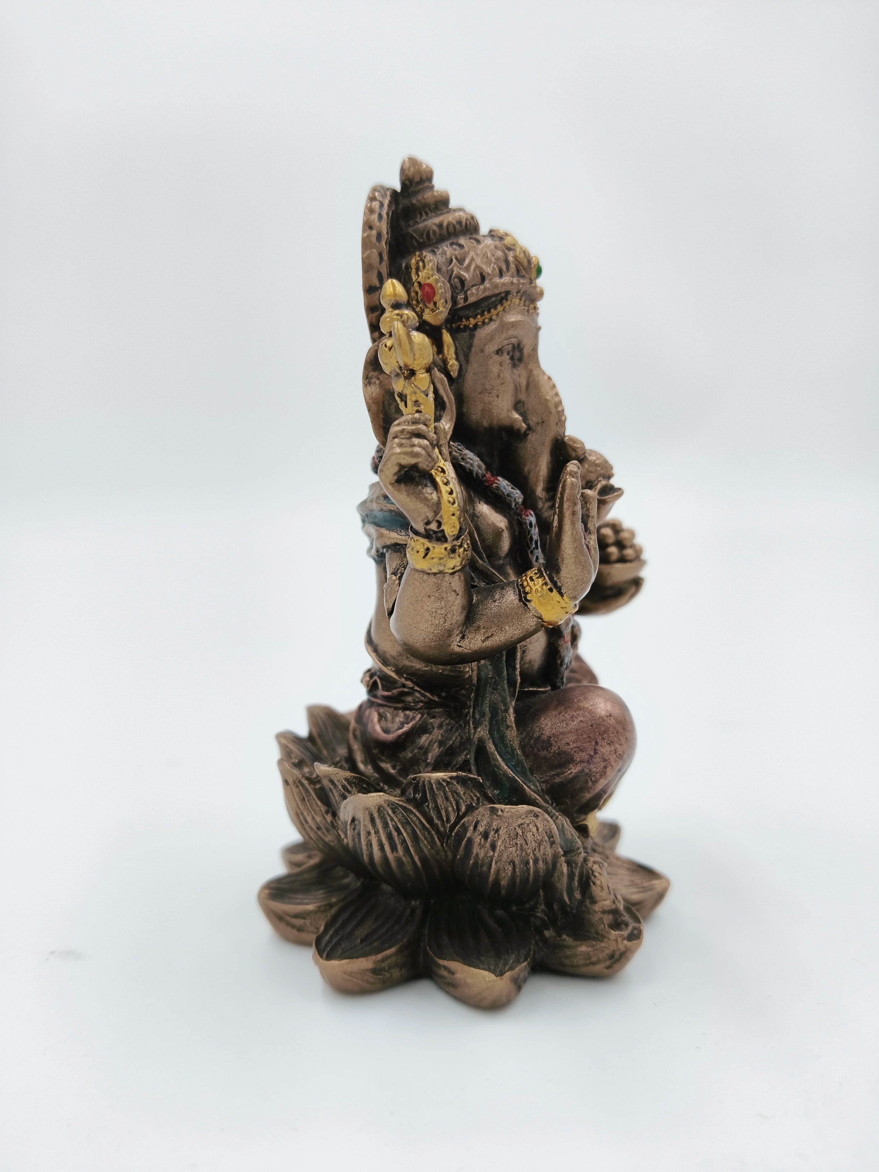 Side view of small polyresin Ganesh statue seated on lotus base with gold accents