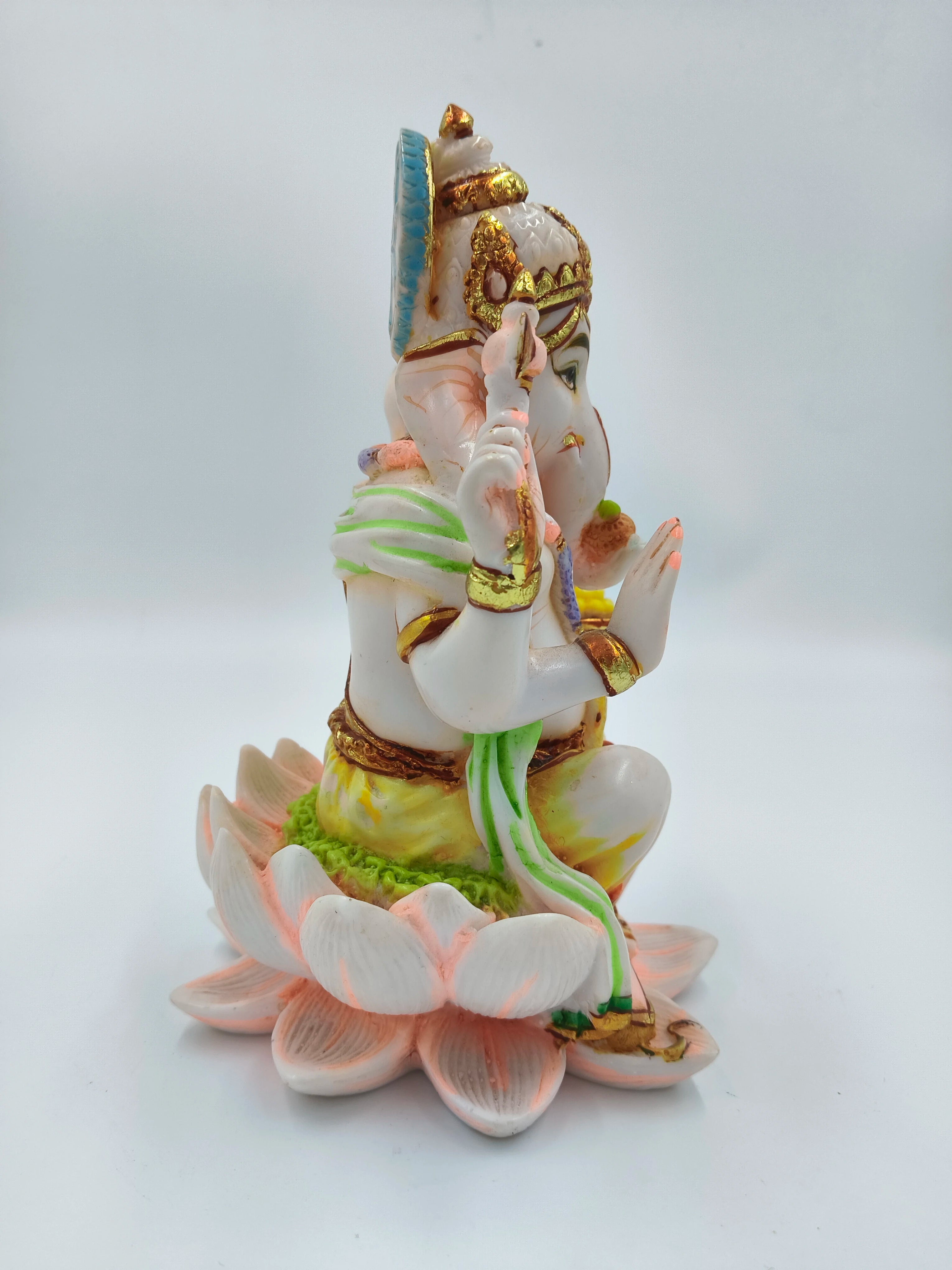 Side view of polyresin Ganesh sculpture seated on lotus flower with detailed ornaments
