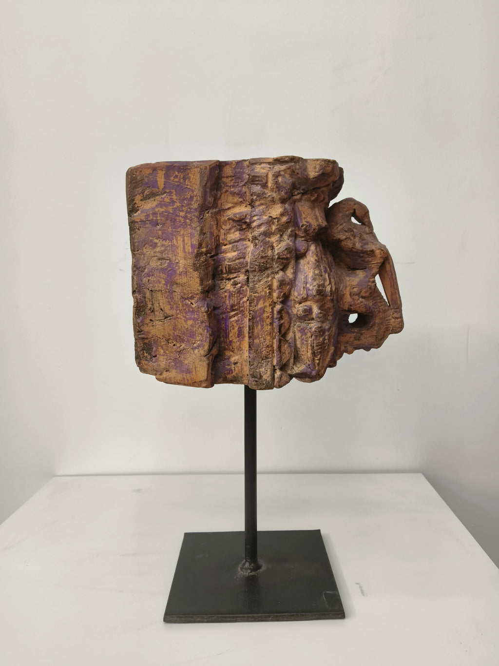 Side view of large weathered wooden sculpture on black metal stand