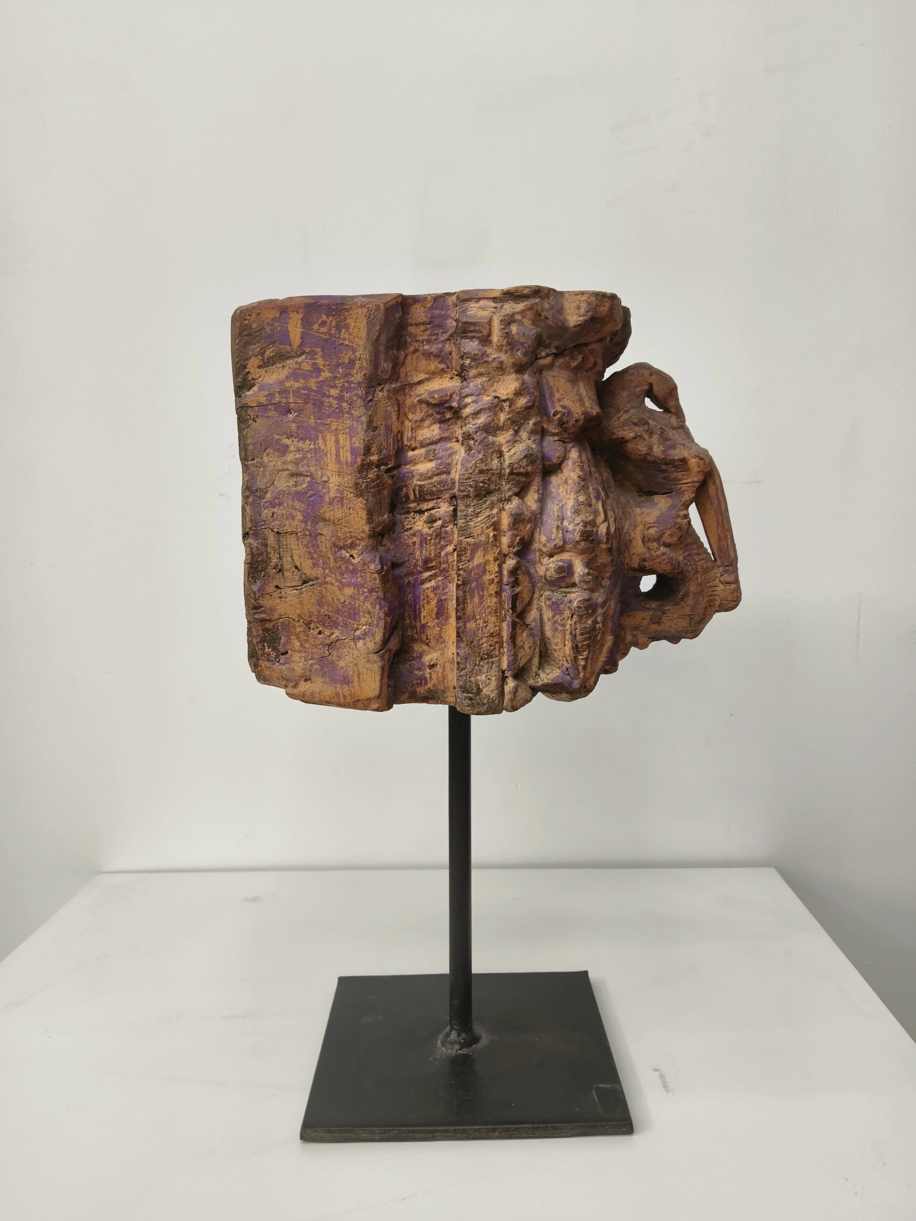 Side view of large weathered wooden sculpture on black metal stand