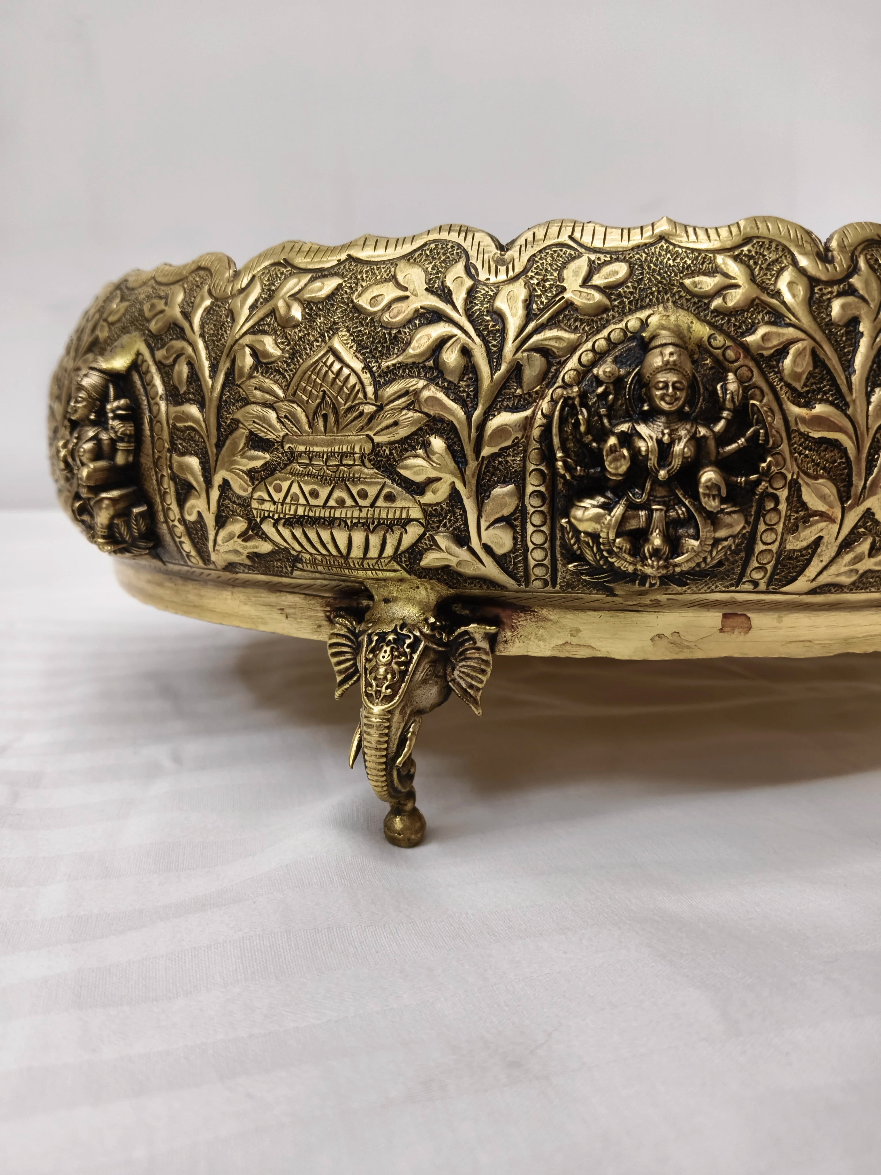 Close-up of brass Astalakshmi urli with floral patterns and elephant foot stand