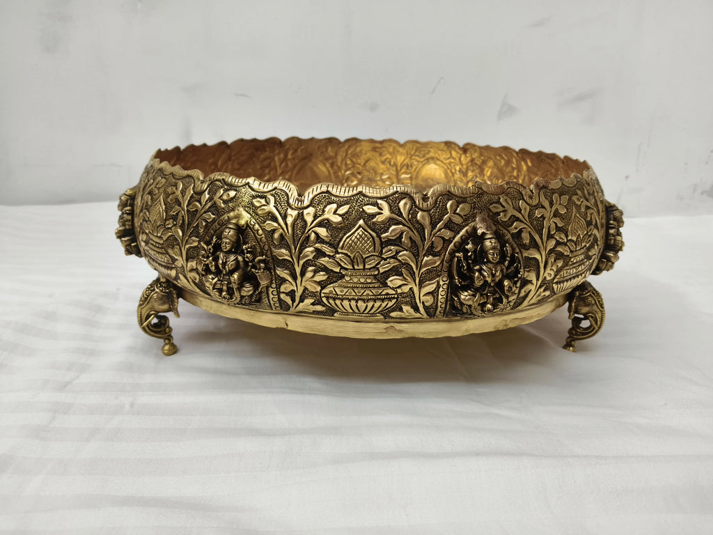 Medium brass Astalakshmi urli with ornate carvings and figurines on three-legged base