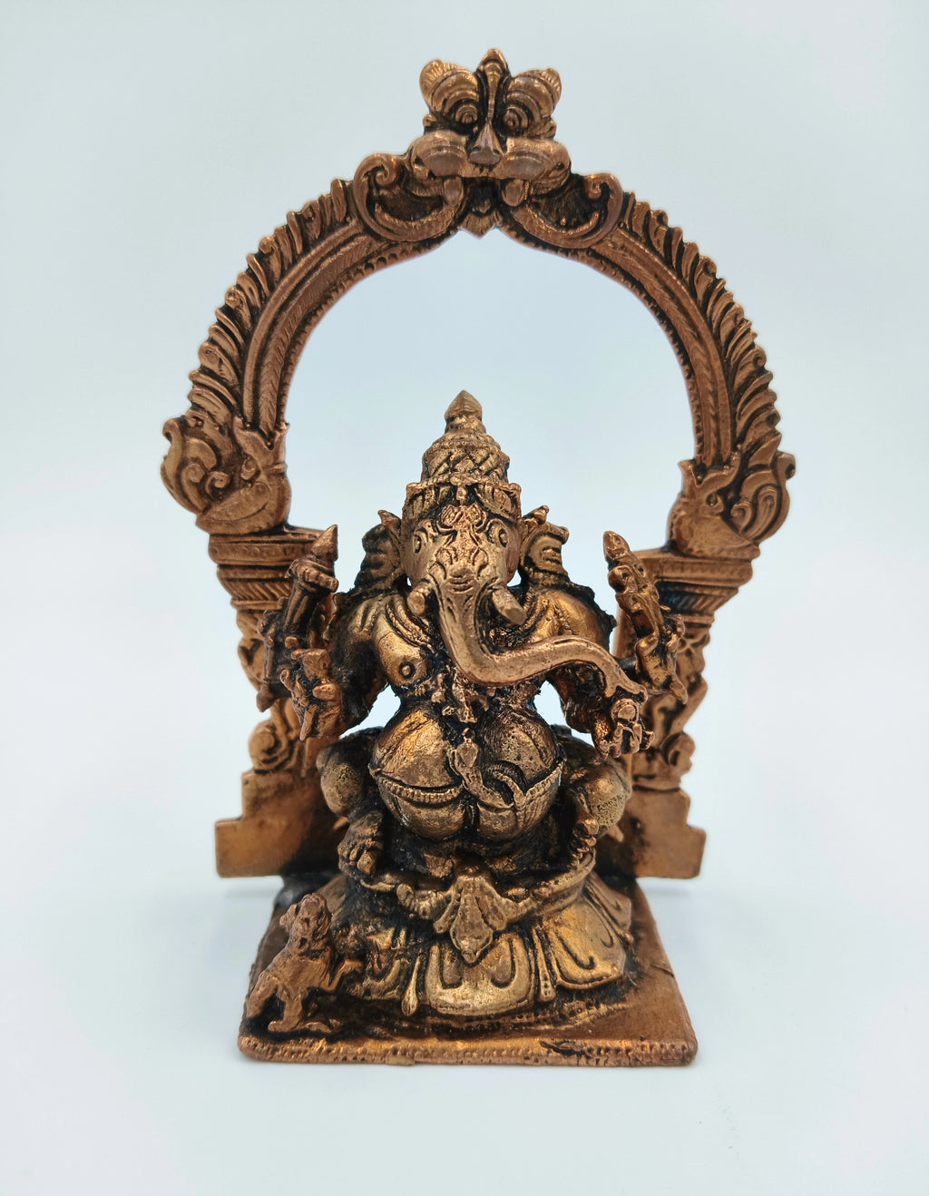 Copper-colored brass Ganesh idol seated with decorative arch behind