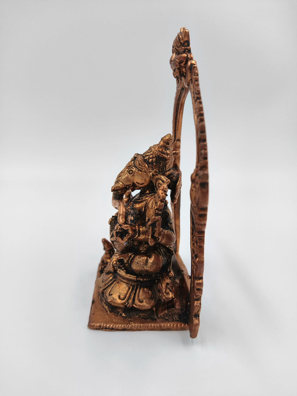 Side view of brass Ganesh statue seated with decorative arch background