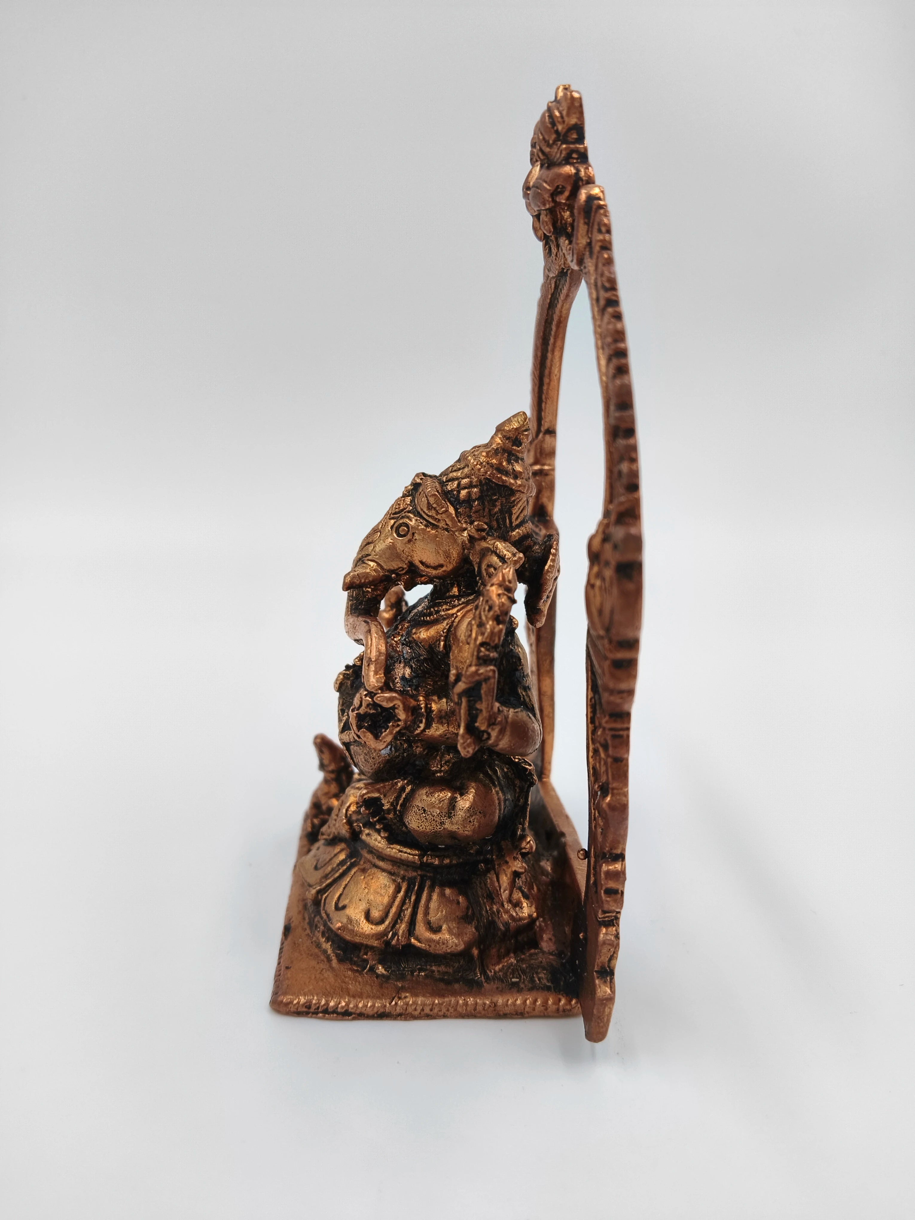 Side view of brass Ganesh statue seated with decorative arch background