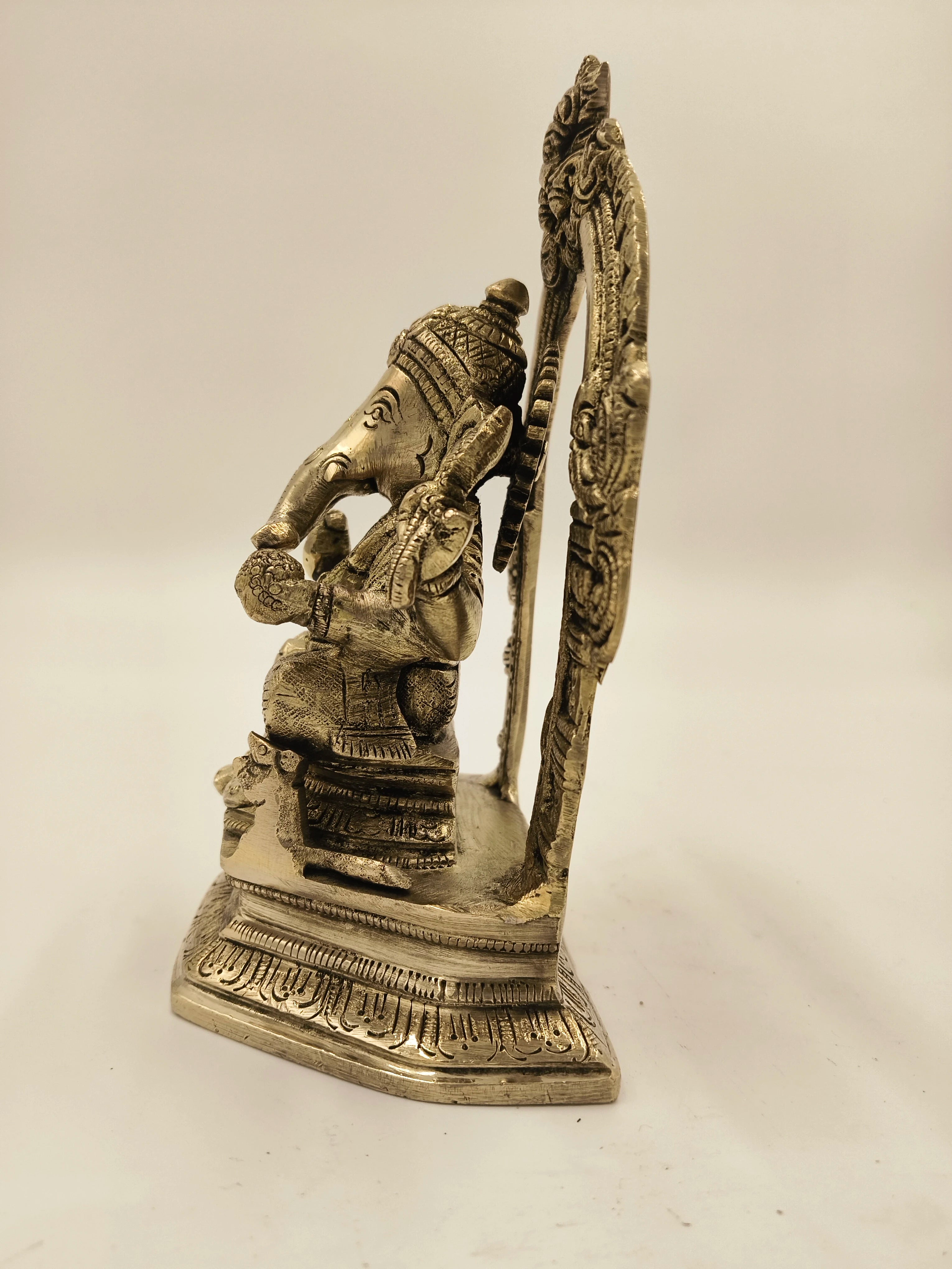 Side view of brass Ganesh sculpture seated on ornate base with decorative arch