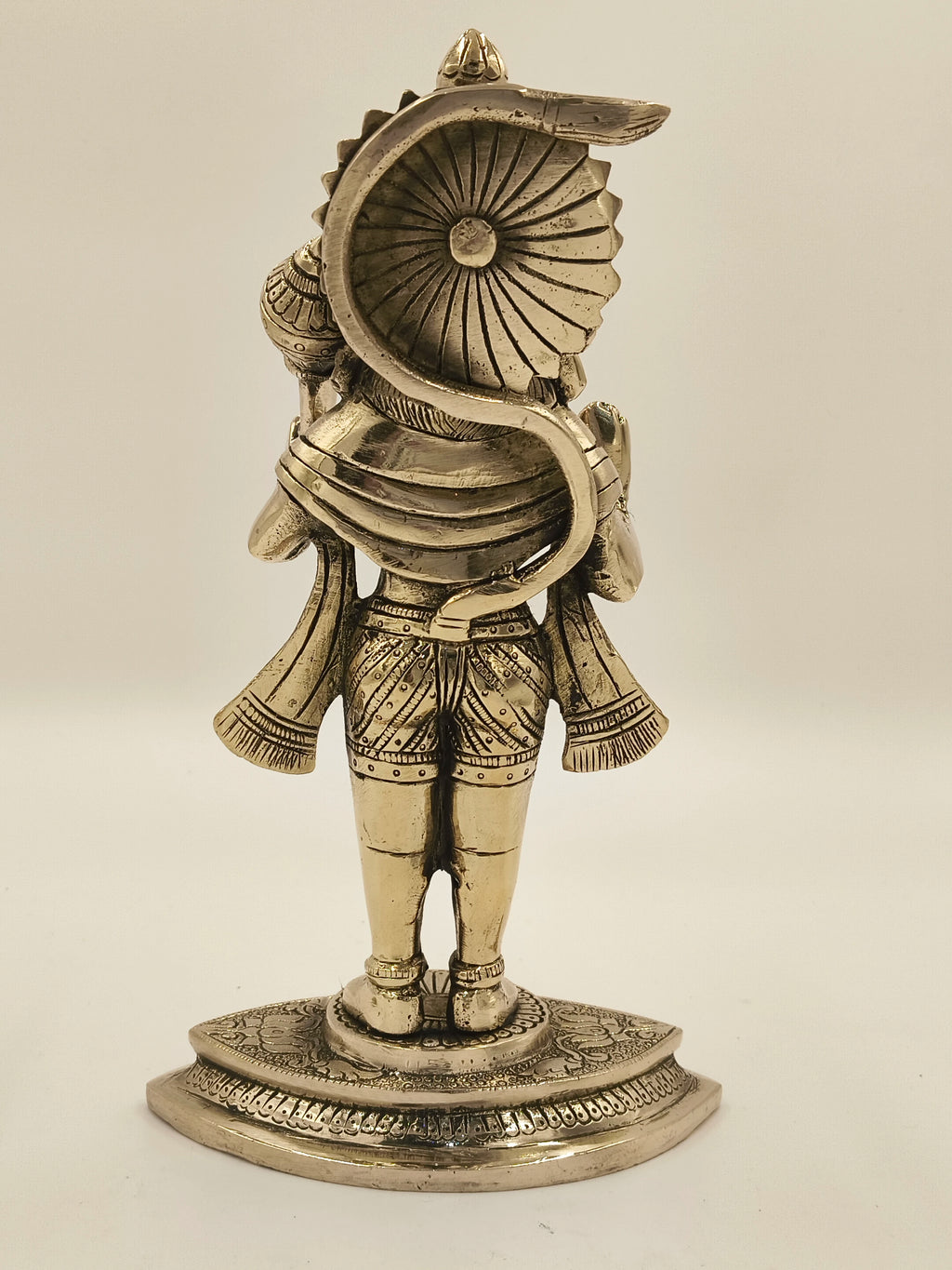 Back view of a large brass Hanuman statue with intricate detailing on a decorated base