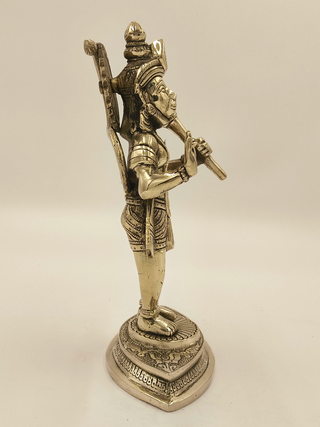 Side view of brass statue of Hanuman holding a mace on decorative base