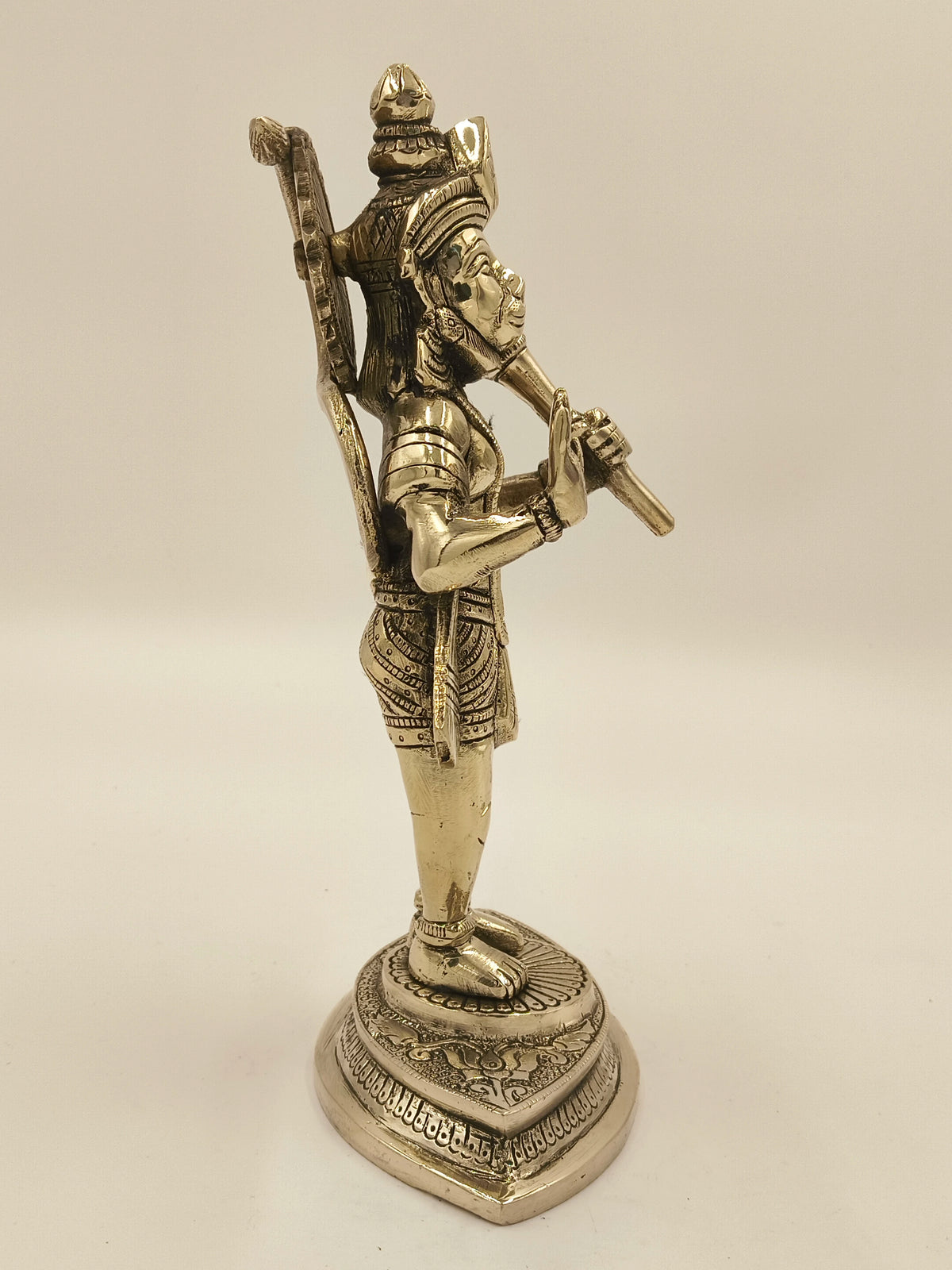 Side view of brass statue of Hanuman holding a mace on decorative base