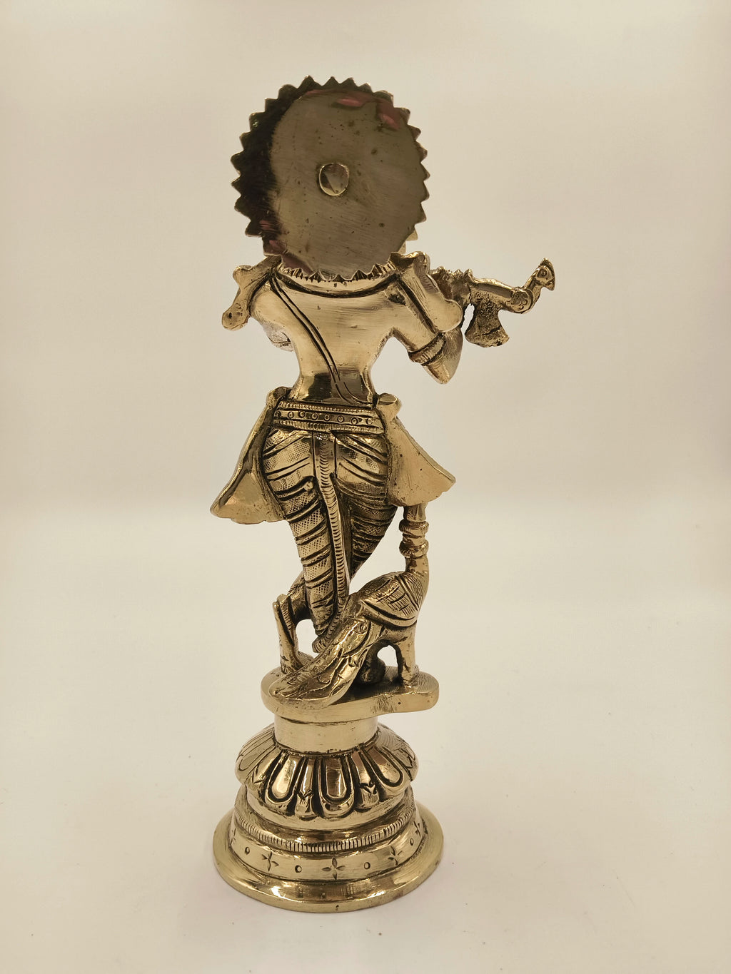 Back view of large brass Krishna figurine playing flute with peacock