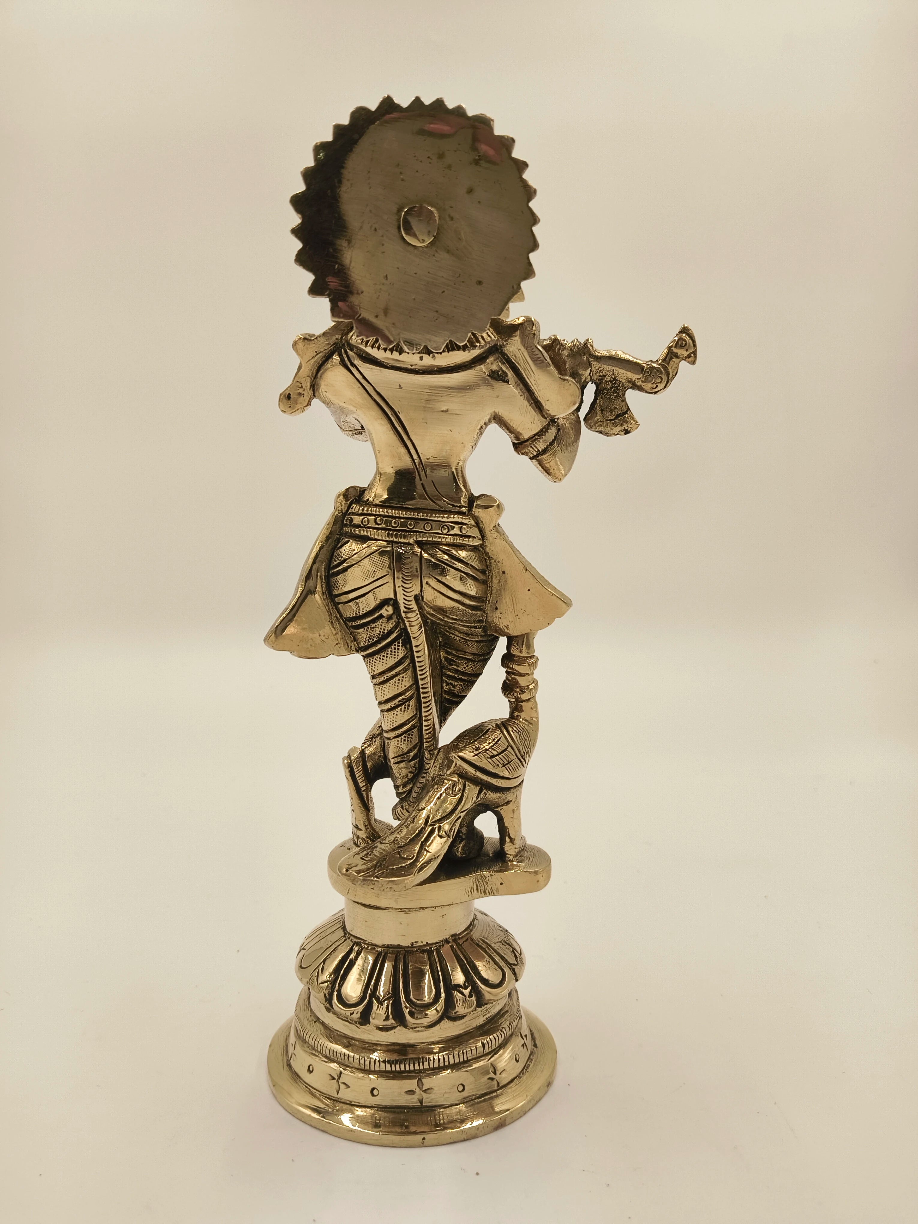 Back view of large brass Krishna figurine playing flute with peacock