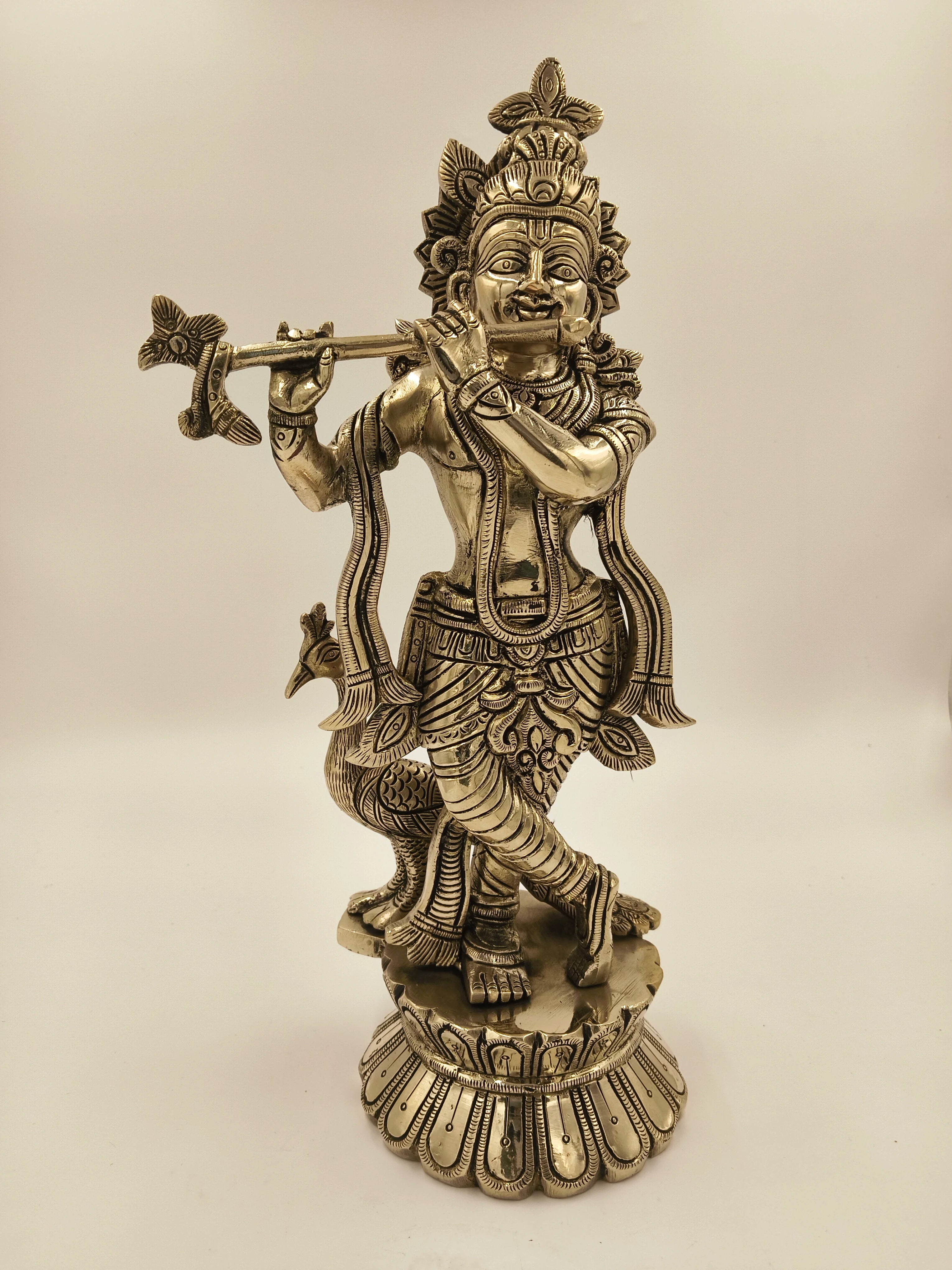 Large brass statue of Krishna playing flute with peacock beside him