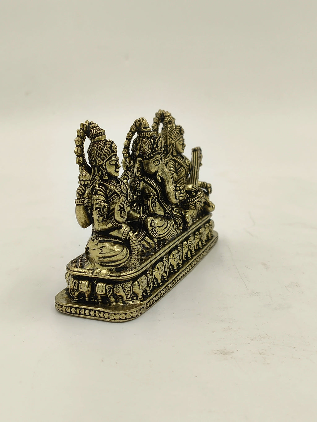Brass sculpture of Lakshmi, Ganesh, and Saraswathi seated side by side