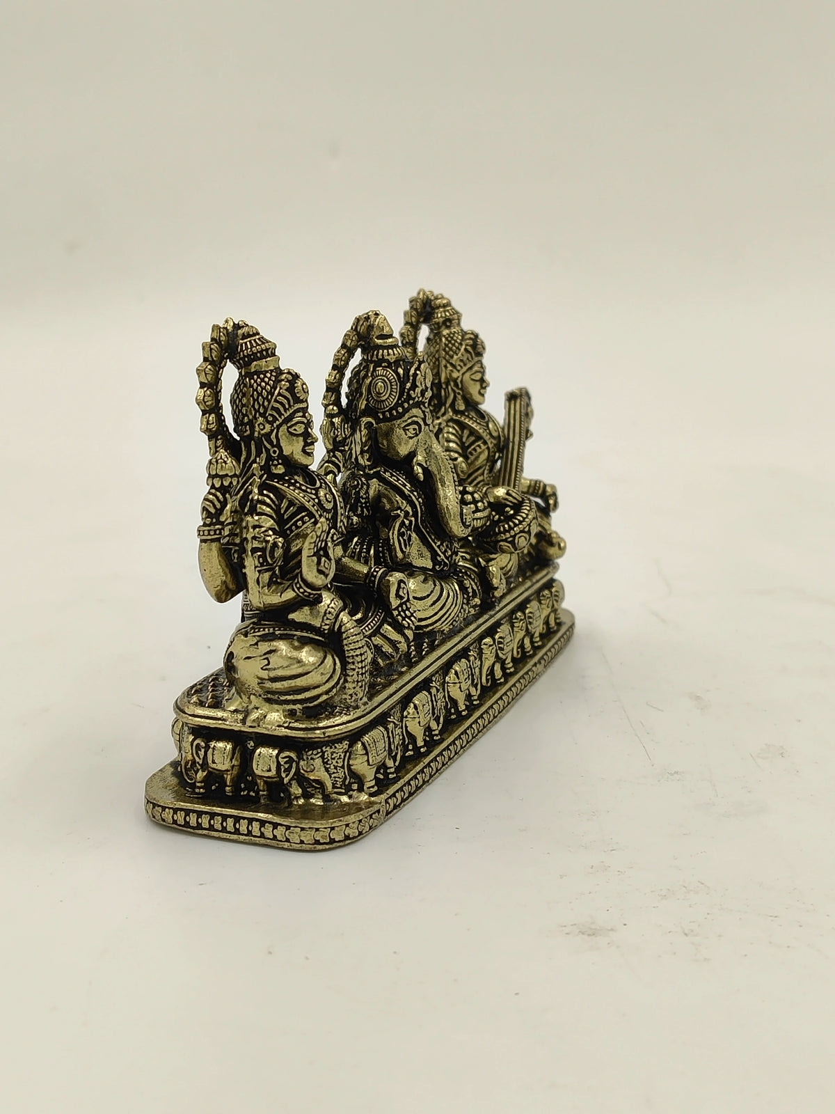 Brass sculpture of Lakshmi, Ganesh, and Saraswathi seated side by side