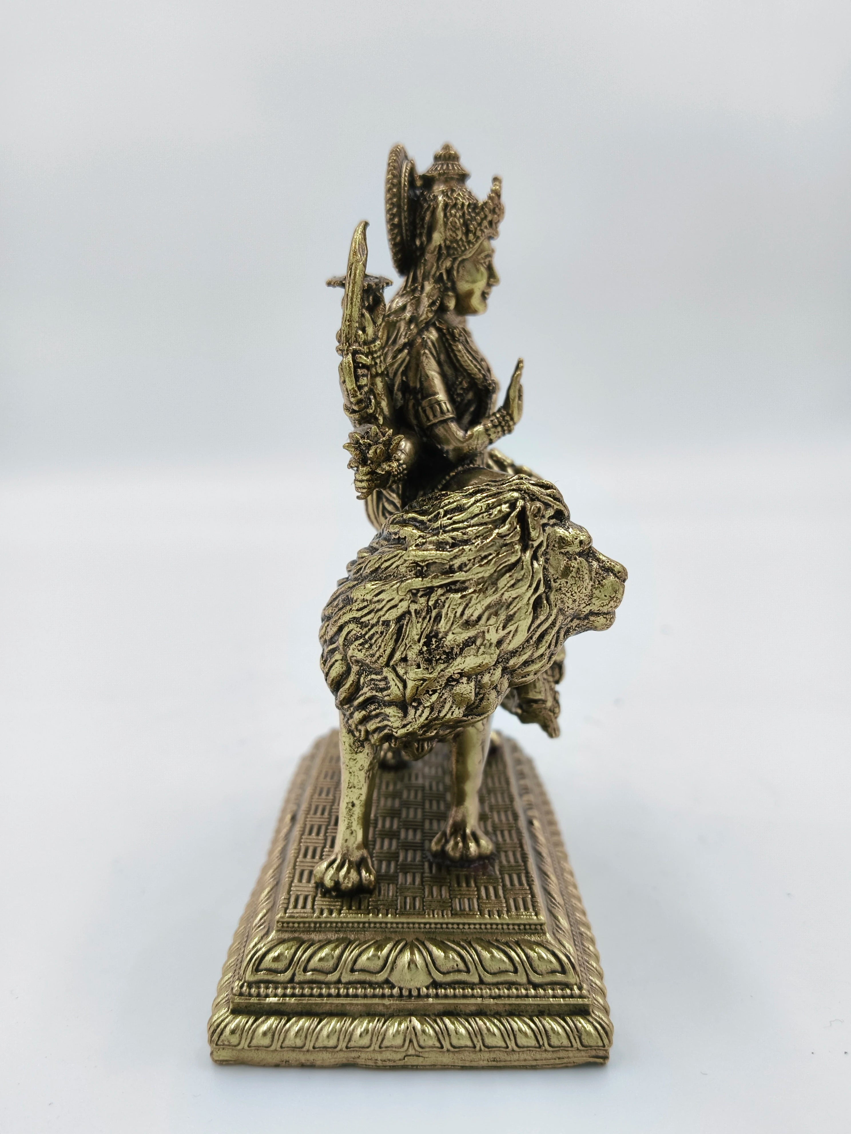 Side view of brass Durga statue seated on a detailed lion base