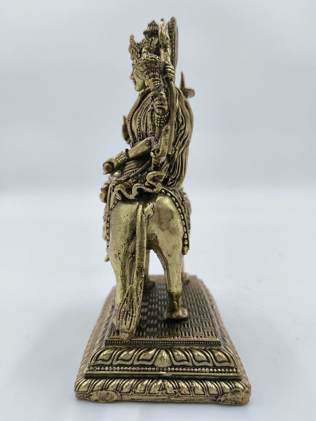 Side view of a medium brass Durga statue seated on a lion with detailed base