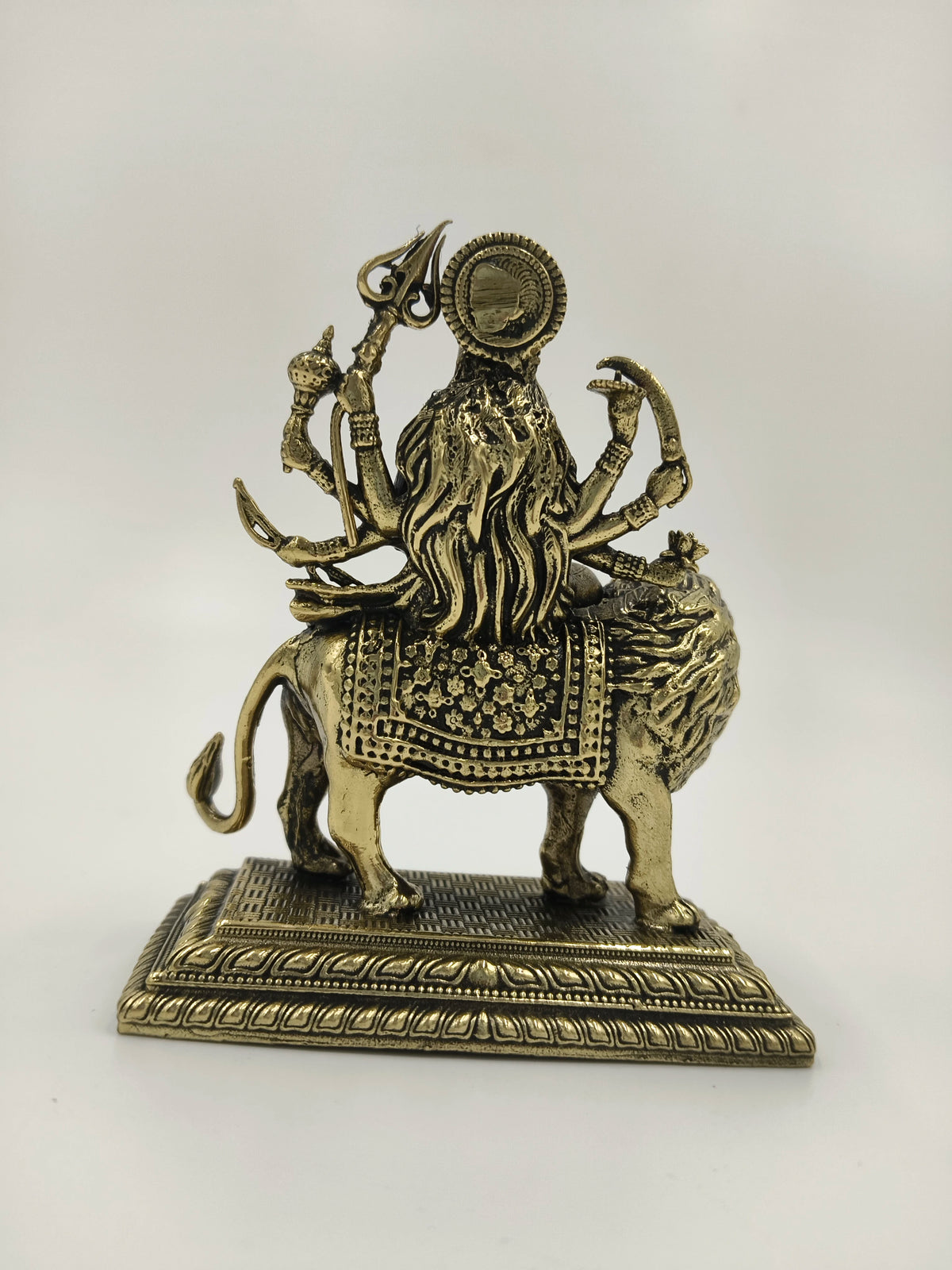 Small brass sculpture of Durga goddess with multiple arms on a lion, rear view