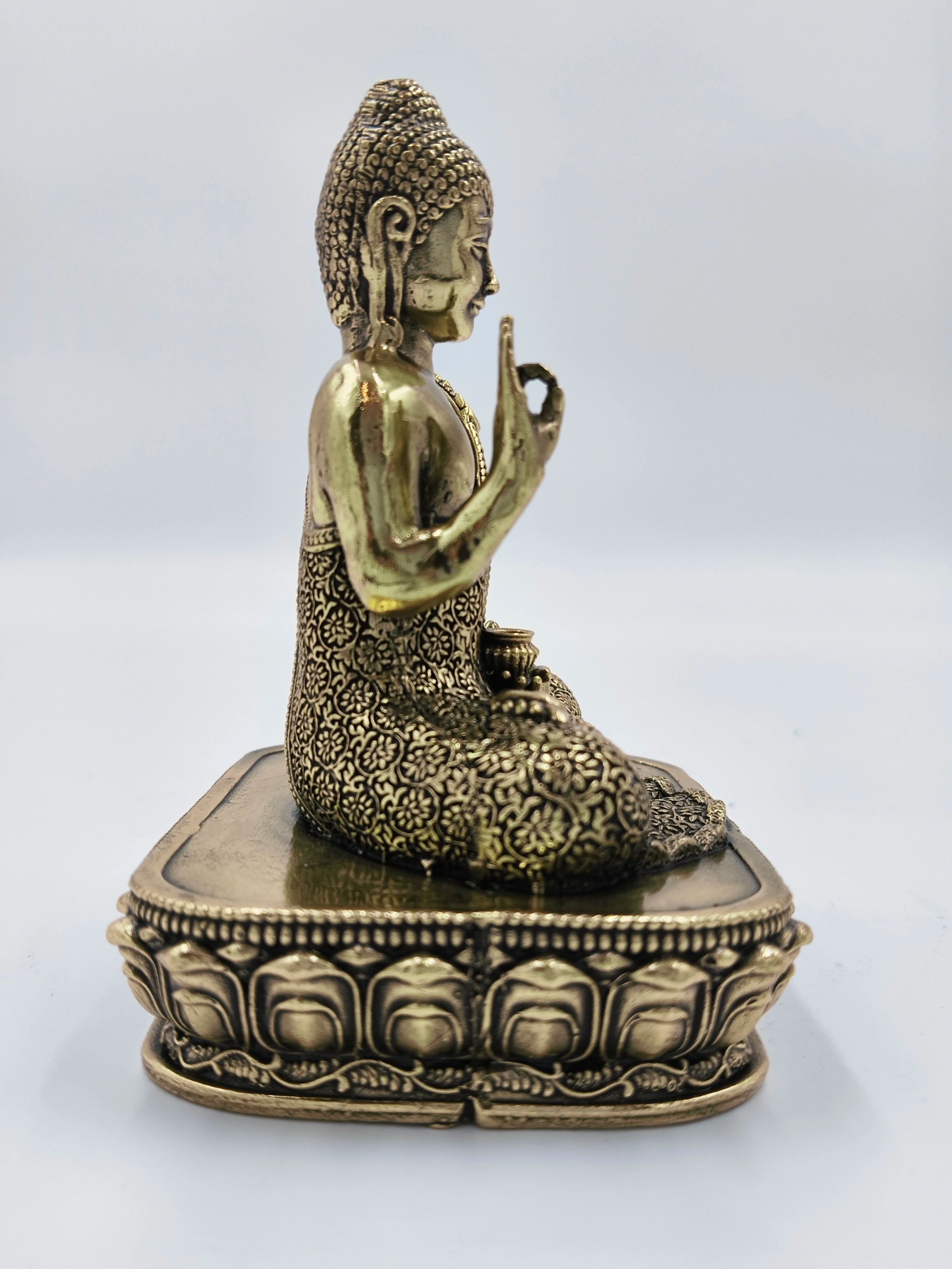 Side view of small brass Buddha statue seated on ornate rectangular base
