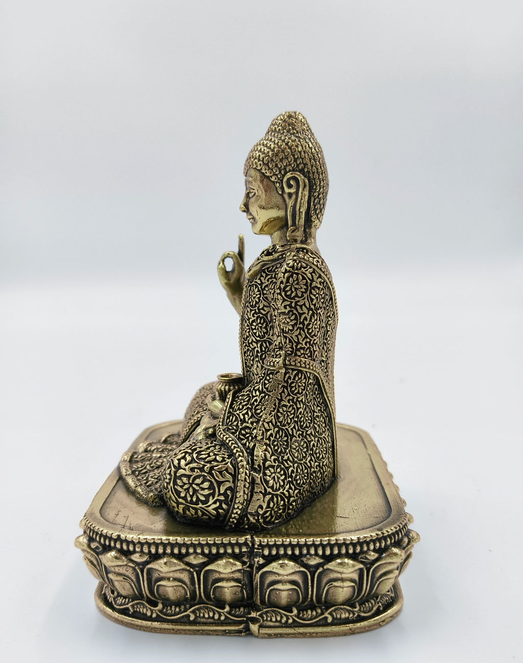 Side view of small brass Buddha figurine seated on lotus base with detailed floral patterns