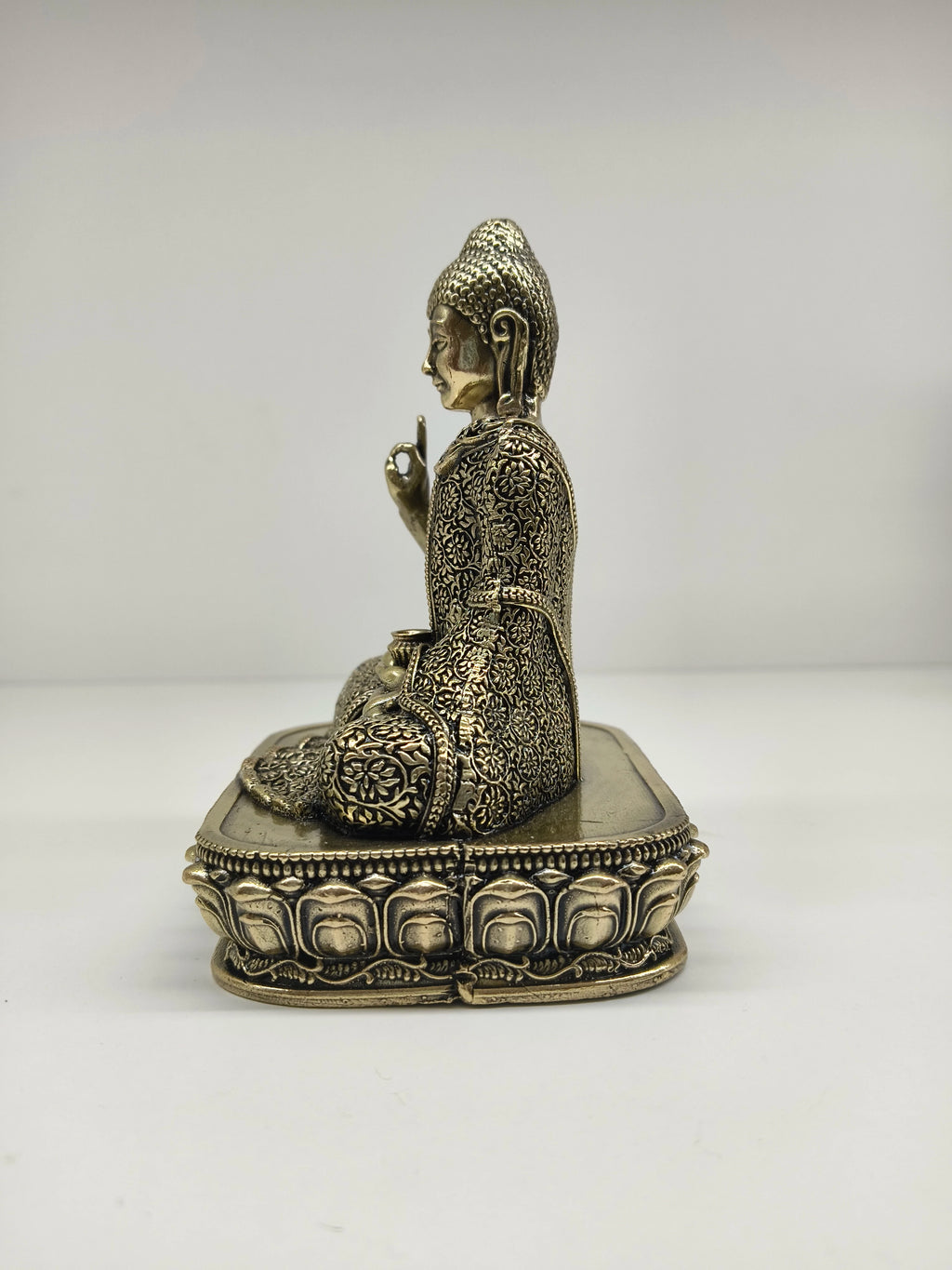 Side view of small brass Buddha statue with intricate floral patterns