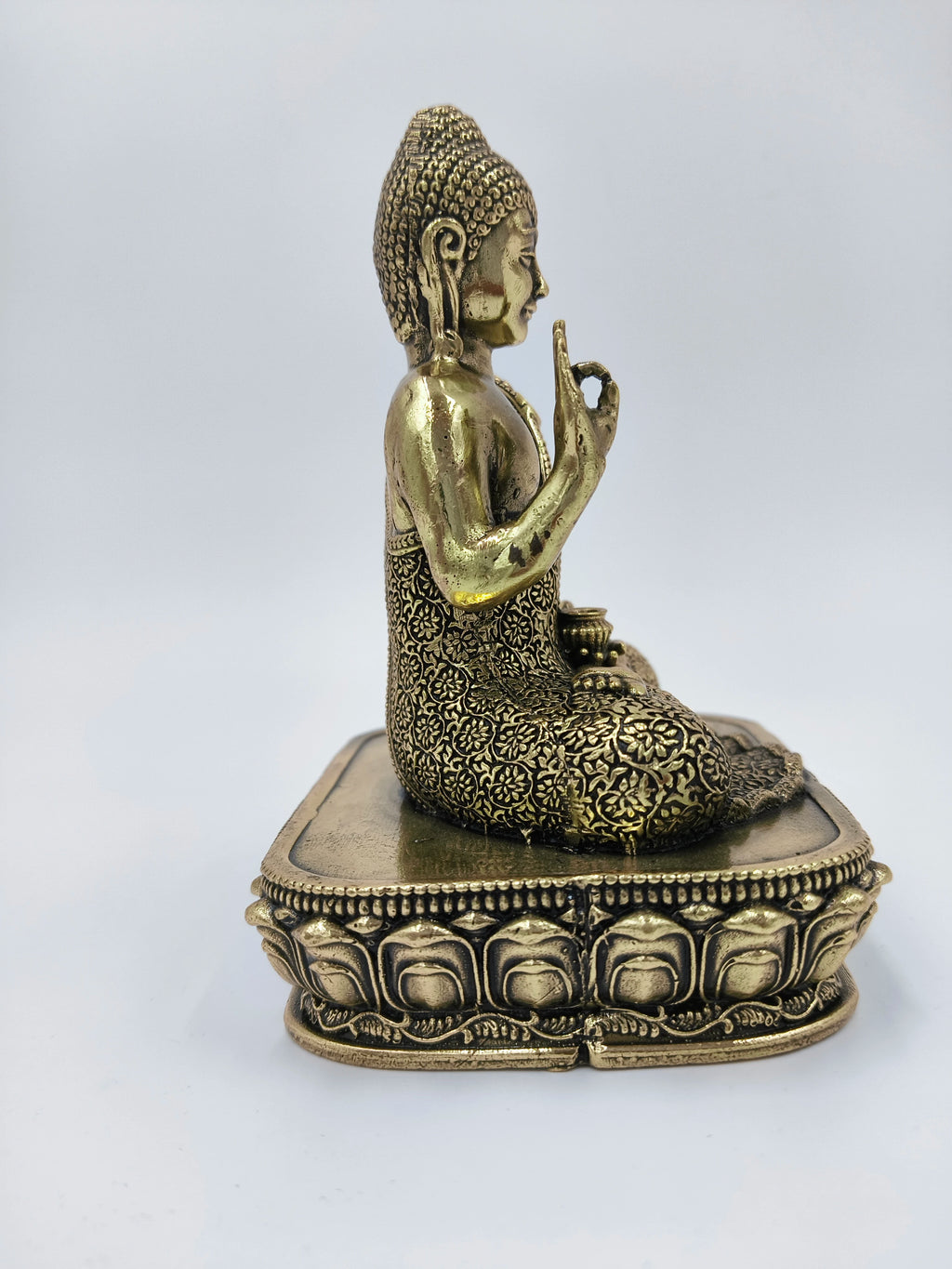 Side view of small brass Buddha statue with intricate floral patterns