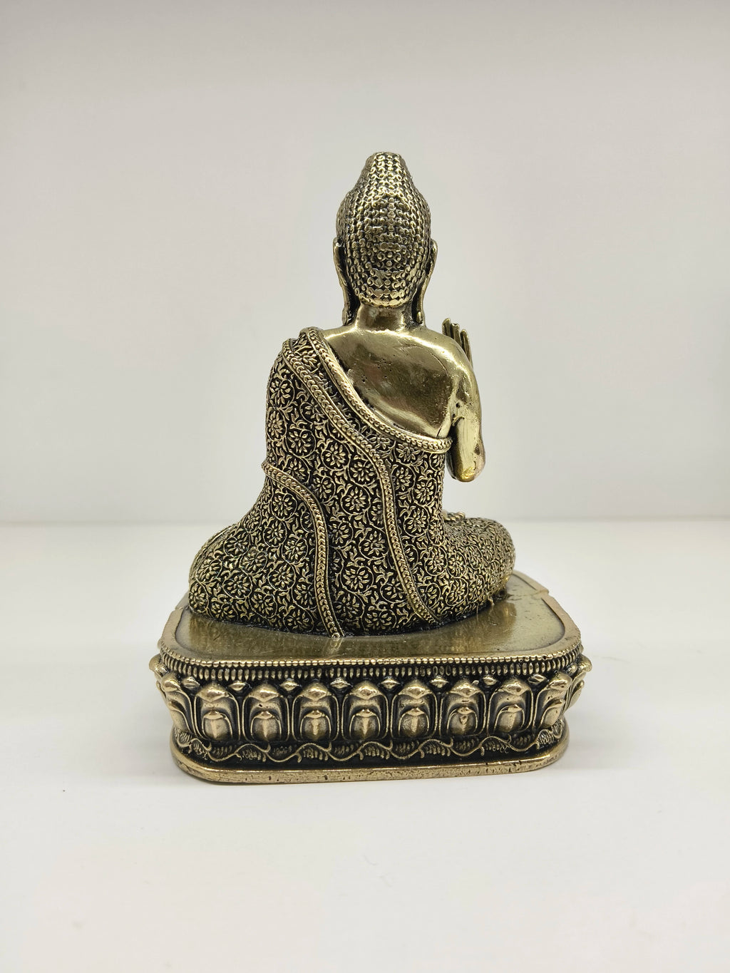 Back view of small brass Buddha statue with intricate patterned robe on ornate base